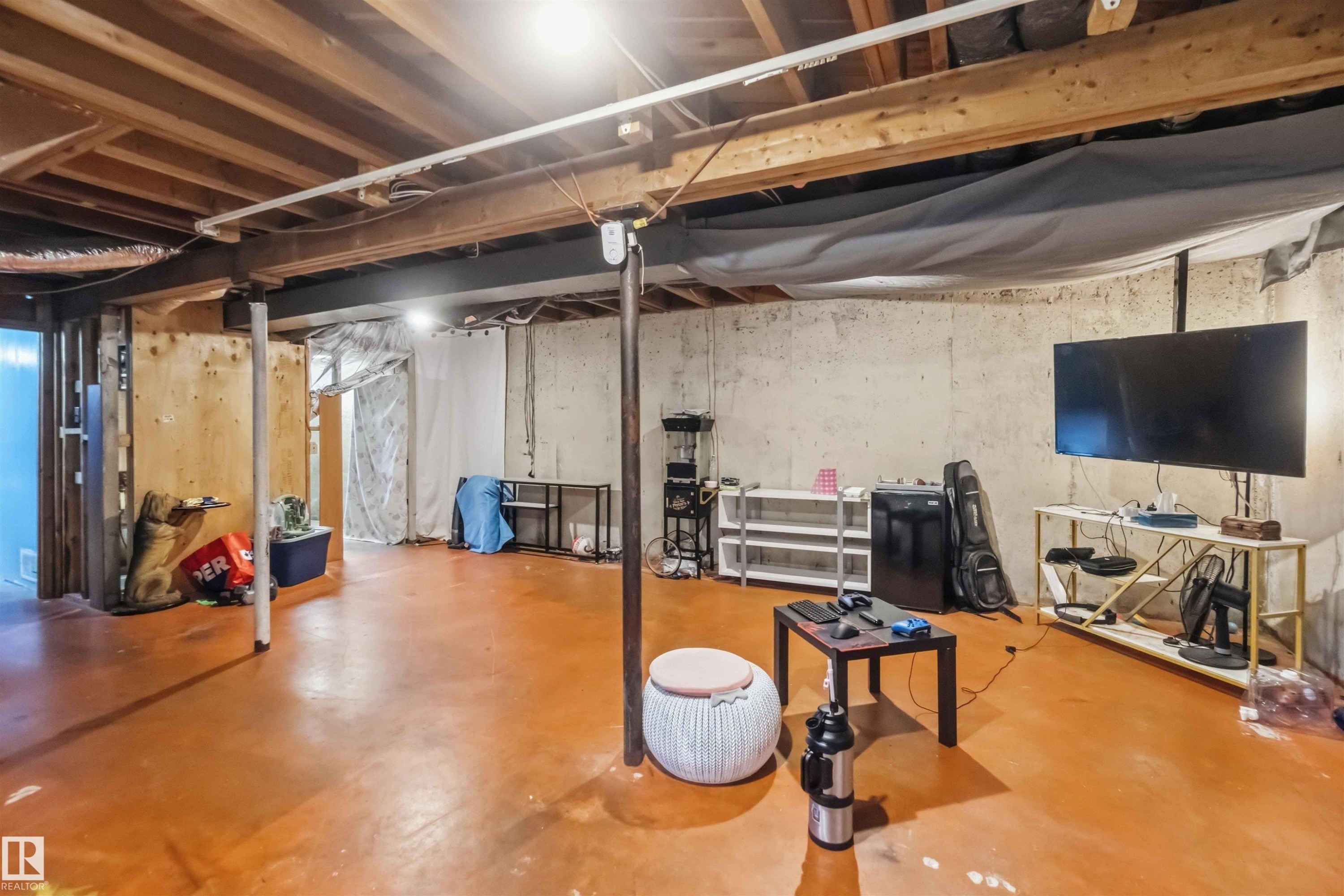 Unfinished basement featuring exposed wood joists, concrete walls, and painted concrete flooring - 13408 67 Street Nw, Edmonton, AB