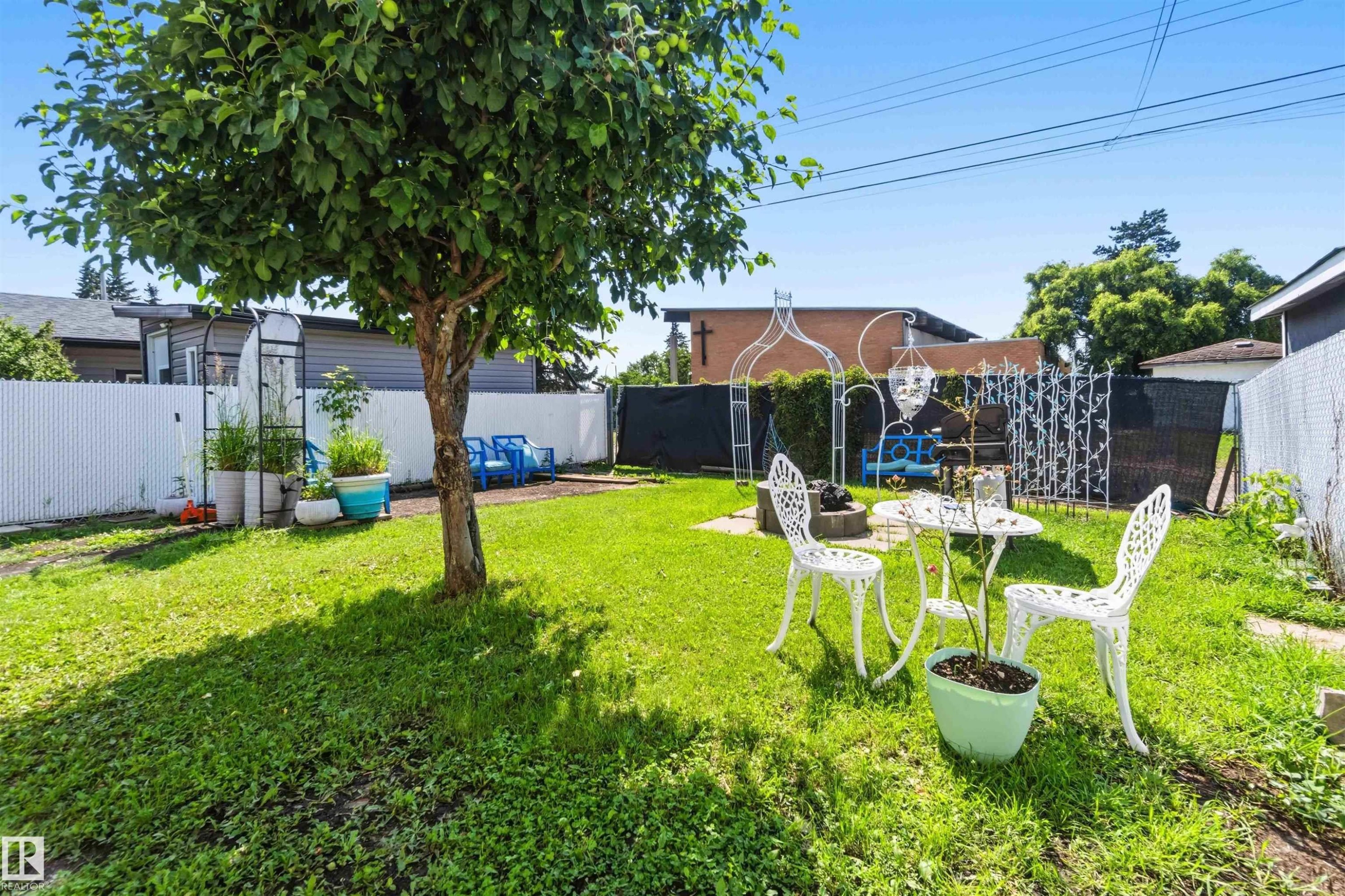 Expansive green space featuring a mature tree, a paved patio area, and perimeter fencing - 13408 67 Street Nw, Edmonton, AB