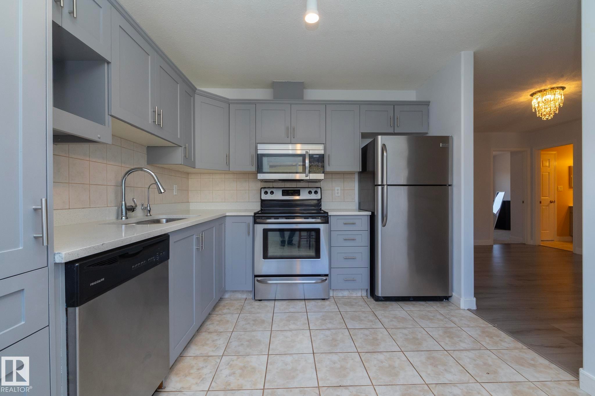 Kitchen featuring gray cabinetry, stainless steel appliances, light-toned countertop, square tile backsplash, and ceramic tile flooring - #37 3811 85 St Nw, Edmonton, AB