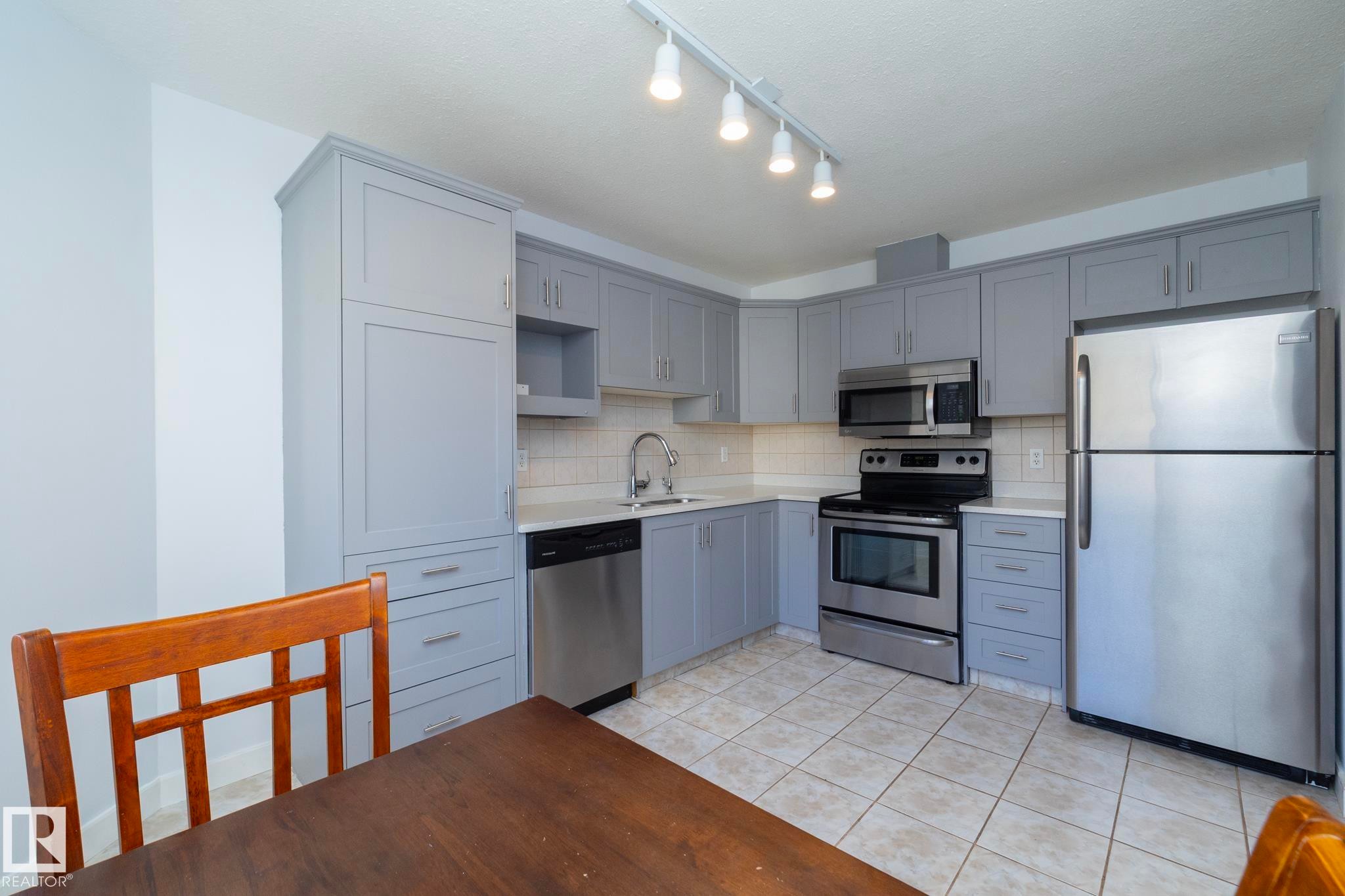 Kitchen featuring light gray cabinetry, white countertops, stainless steel appliances, ceramic tile flooring, and a white subway tile backsplash - #37 3811 85 St Nw, Edmonton, AB