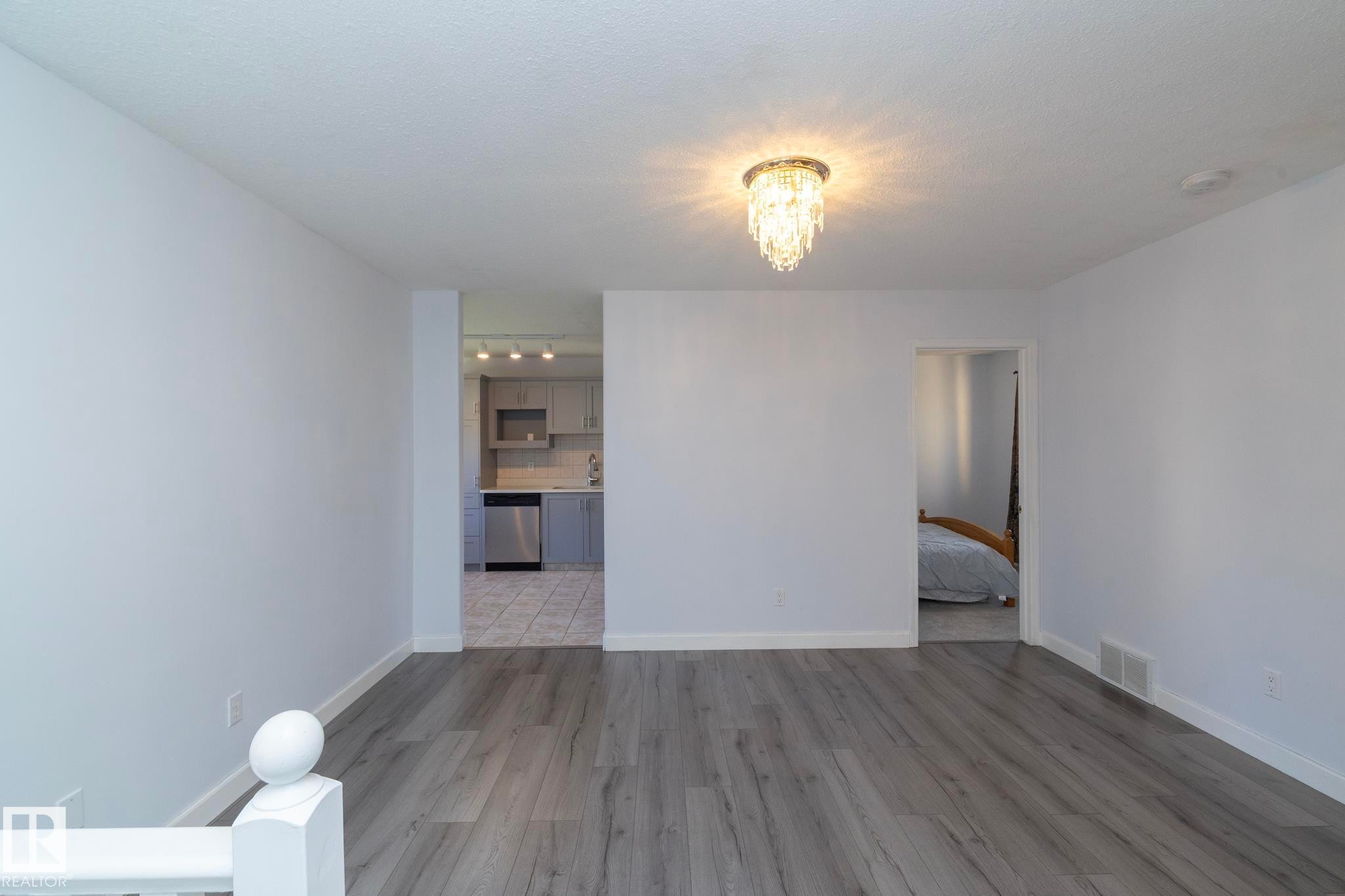 Wood-finish flooring throughout, complemented by light-toned walls and a modern chandelier - #37 3811 85 St Nw, Edmonton, AB