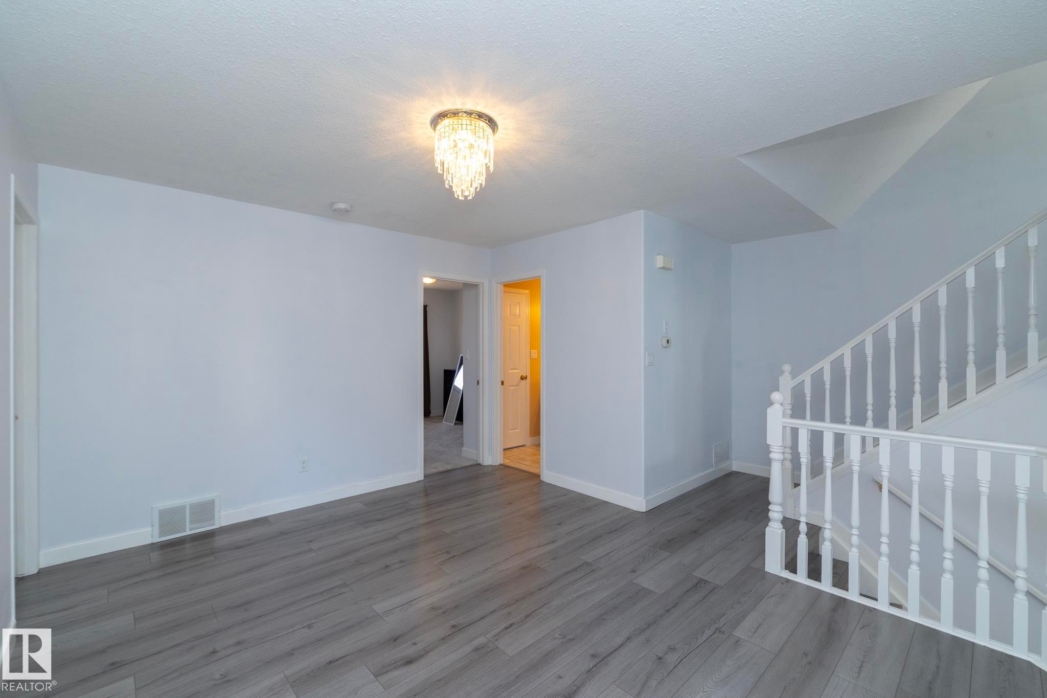 Wood-finish flooring, white painted walls, white trim, and an overhead chandelier with decorative accents - #37 3811 85 St Nw, Edmonton, AB