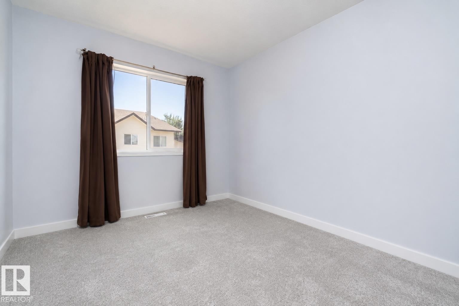 Bright secondary bedroom with neutral carpet flooring, white walls, and large window with brown thermal curtains - #37 3811 85 St Nw, Edmonton, AB