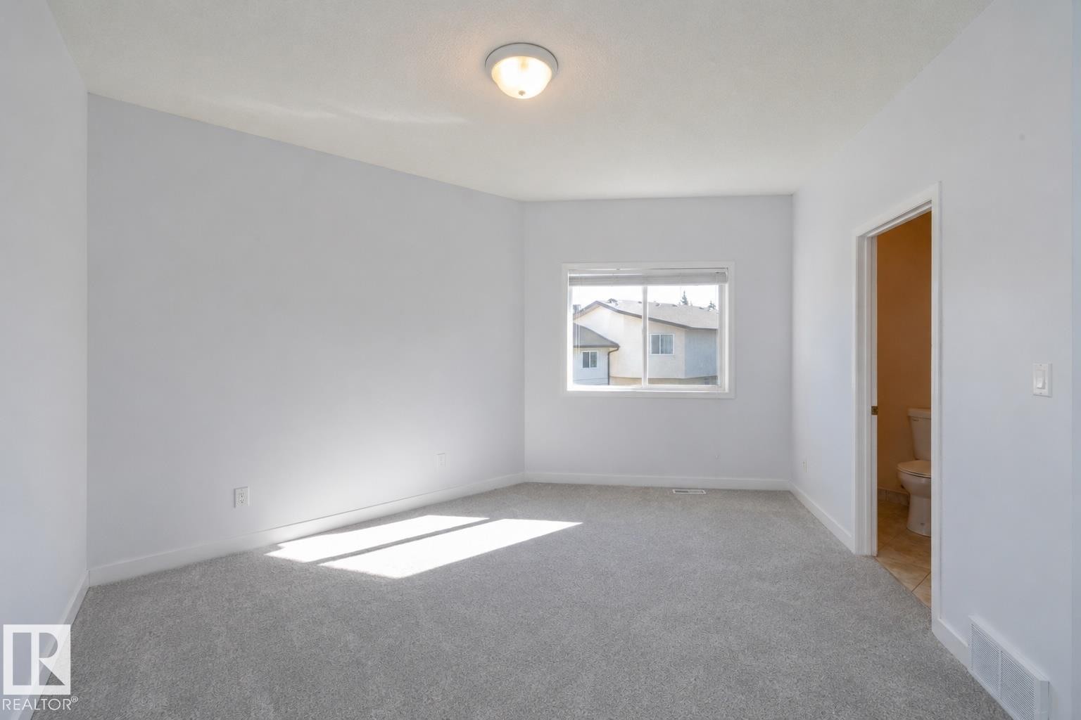 Neutral wall color, light-toned carpeting, ceiling-mounted light fixture, window with exterior views, and an interior door - #37 3811 85 St Nw, Edmonton, AB