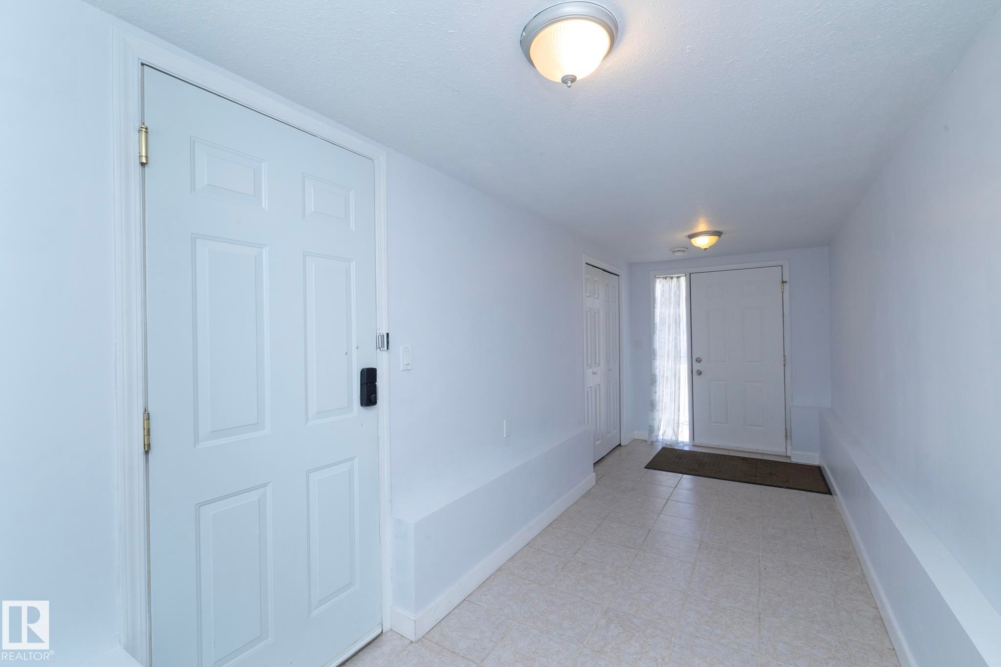Entryway with neutral tile flooring, two ceiling-mounted light fixtures, and white paneled doors - #37 3811 85 St Nw, Edmonton, AB