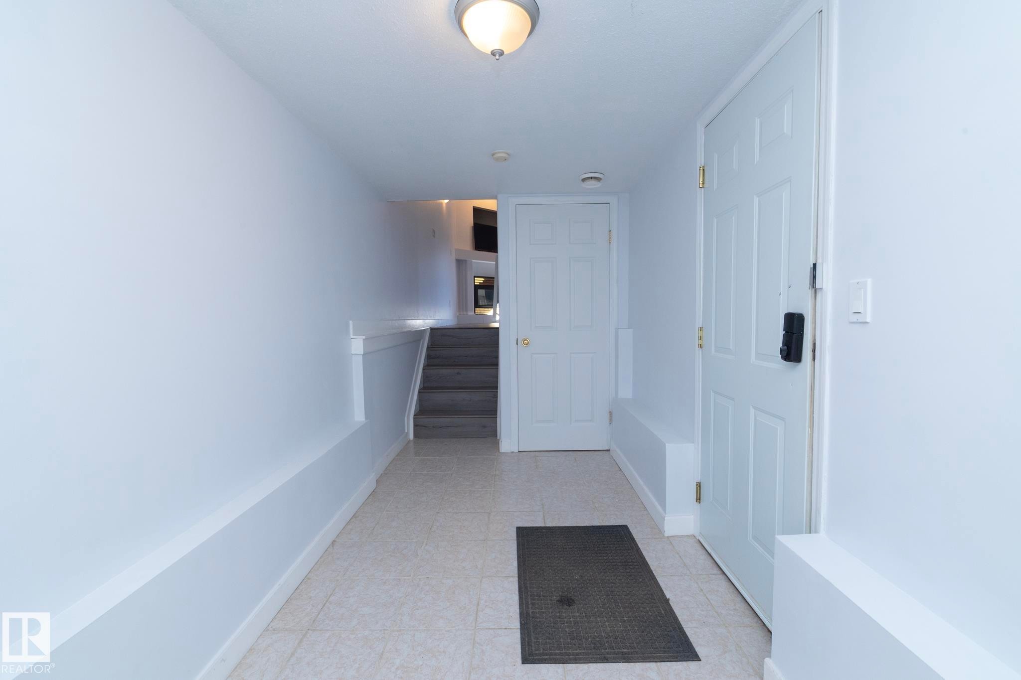 Foyer featuring light-toned tile flooring, white paneled doors, and a staircase with a half-wall railing - #37 3811 85 St Nw, Edmonton, AB