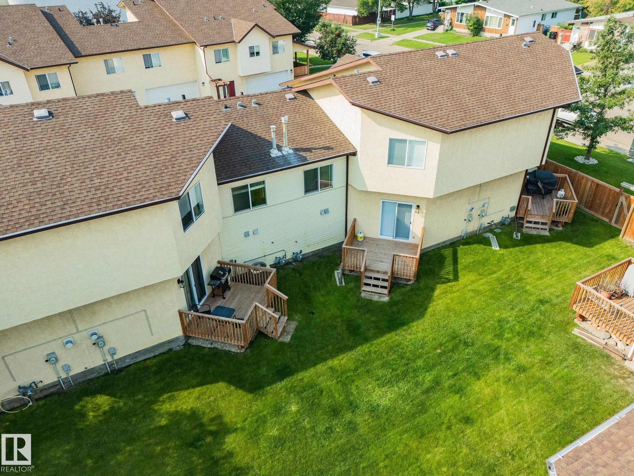 Expansive backyard featuring a manicured lawn, multiple wood decks, and a privacy fence - #37 3811 85 St Nw, Edmonton, AB