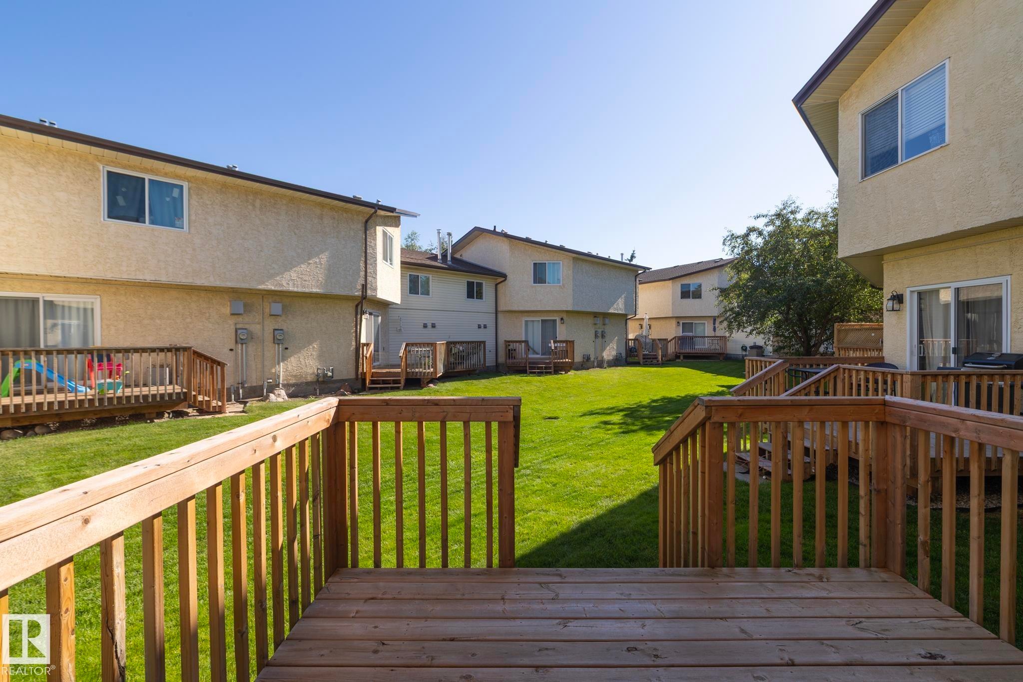 Expansive green lawn surrounded by multiple wood decks with railings - #37 3811 85 St Nw, Edmonton, AB