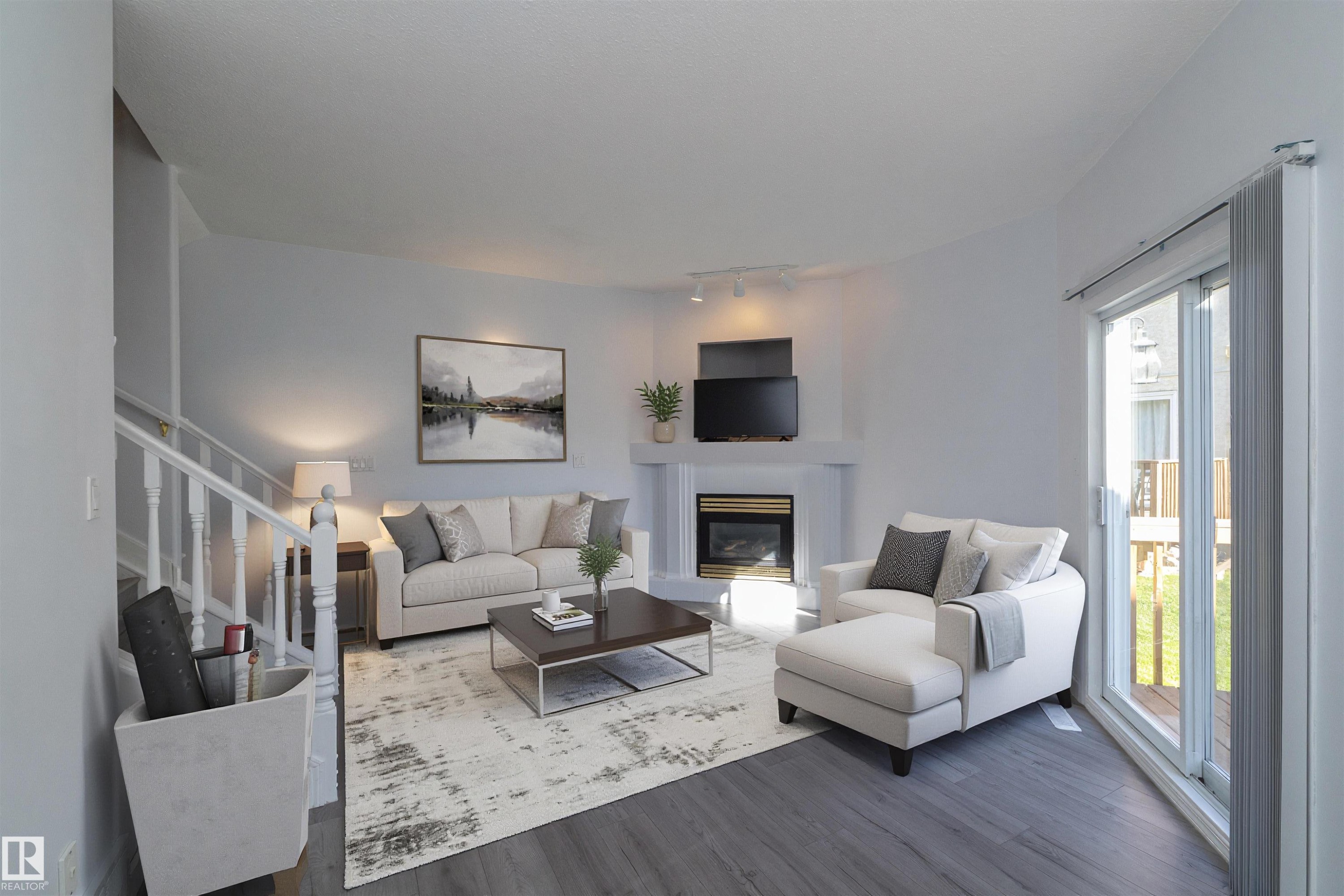 White fireplace with a dark insert, track lighting, light gray walls, wood-finish flooring, and white stair railing - #37 3811 85 St Nw, Edmonton, AB