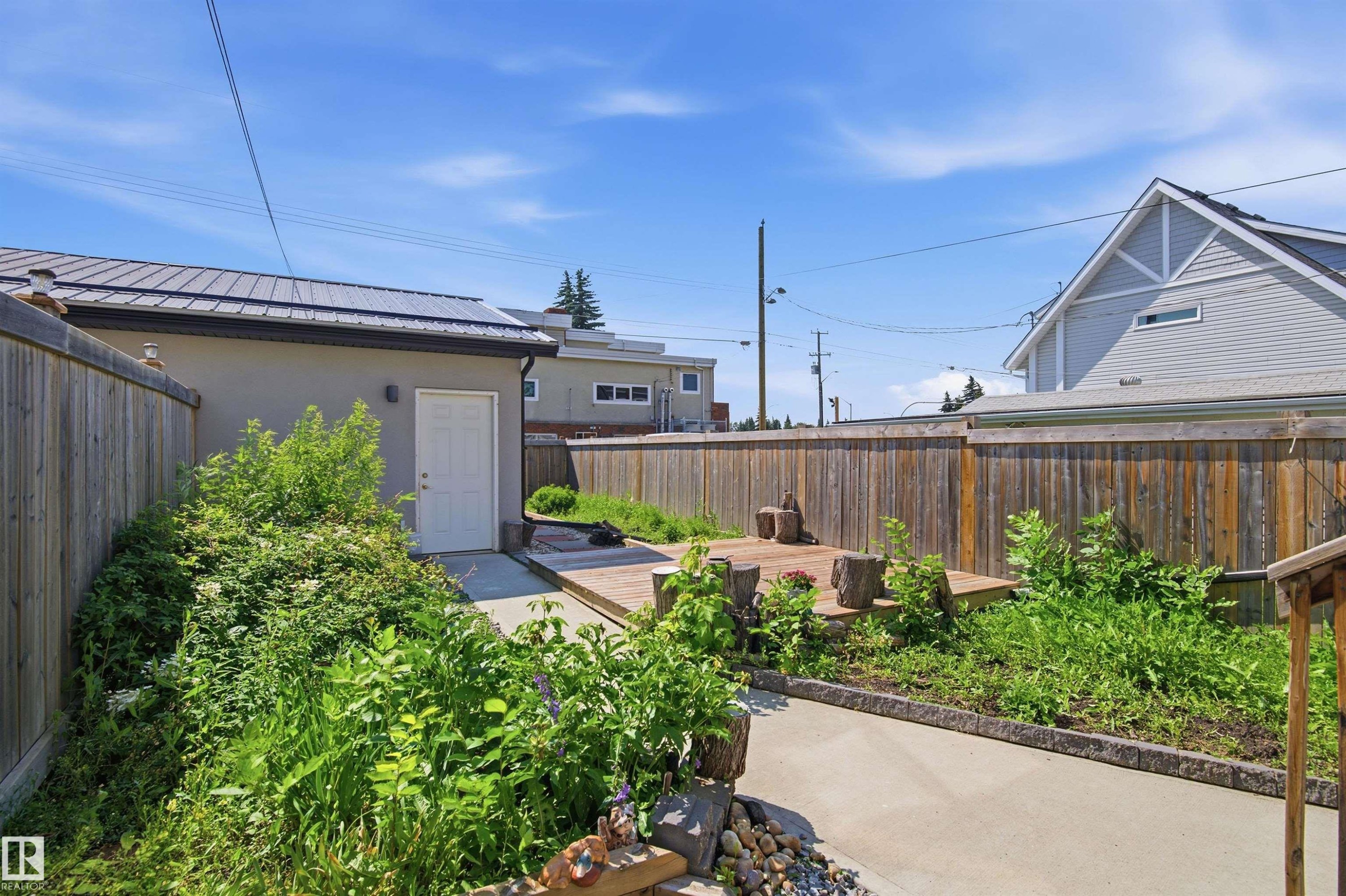 Rear yard featuring a concrete pathway, a wooden fence, and a raised wooden deck - 10833 63 Avenue Nw, Edmonton, AB