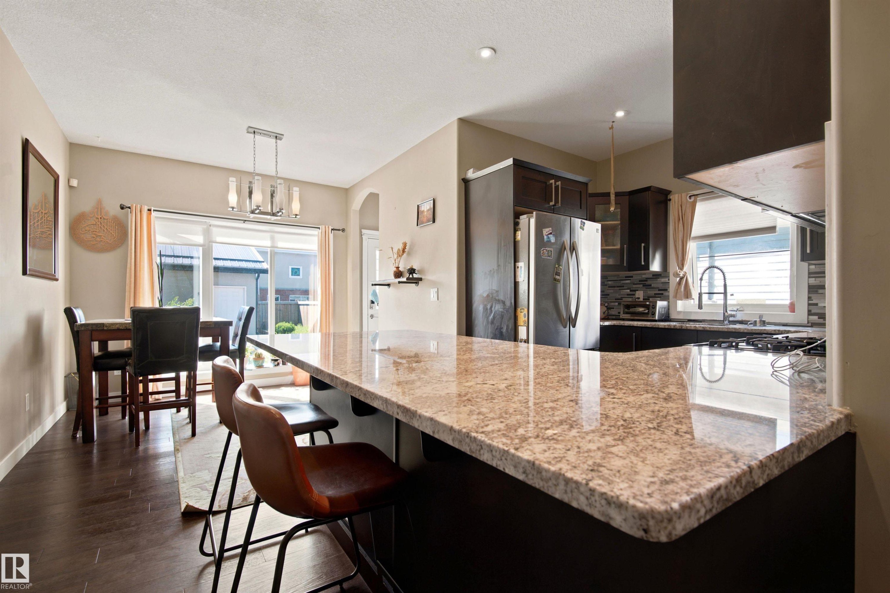 Kitchen featuring granite countertops, dark wood-finish cabinetry, stainless steel appliances, and a tile backsplash - 10833 63 Avenue Nw, Edmonton, AB