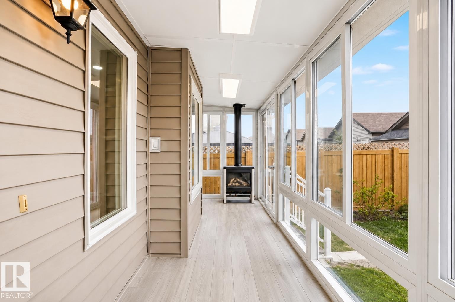 Enclosed sunroom featuring expansive fenestration, wood-finish flooring, a built-in fireplace, and a full-length slatted exterior wall - 445 Watt Boulevard Sw, Edmonton, AB