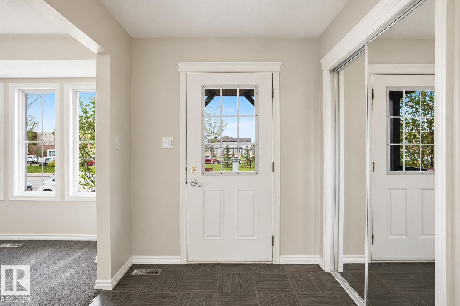 Entryway featuring dark patterned flooring, a white paneled door with windowpanes, and a mirrored closet door - 445 Watt Boulevard Sw, Edmonton, AB