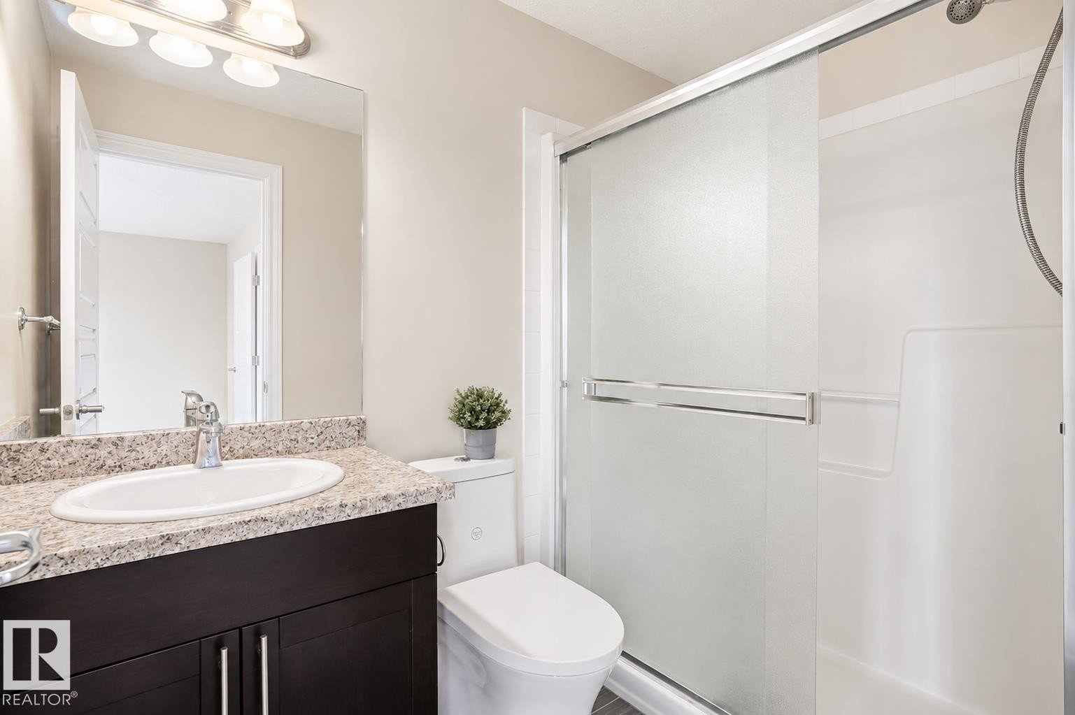 Bathroom featuring a vanity with an oval sink, dark wood-finish cabinetry, a stone-finish countertop, and a shower with frosted glass sliding doors - 445 Watt Boulevard Sw, Edmonton, AB
