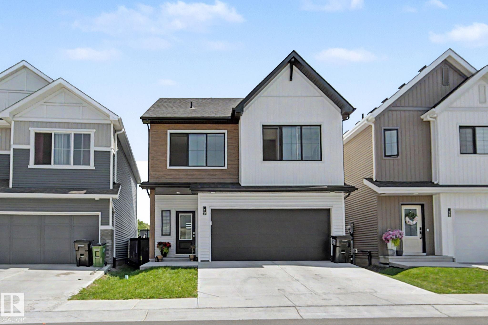 Contemporary two-story residence featuring a striking black and white exterior with wood-look paneling accents - #12 905 172 St Sw, Edmonton, AB - Outdoor With Facade