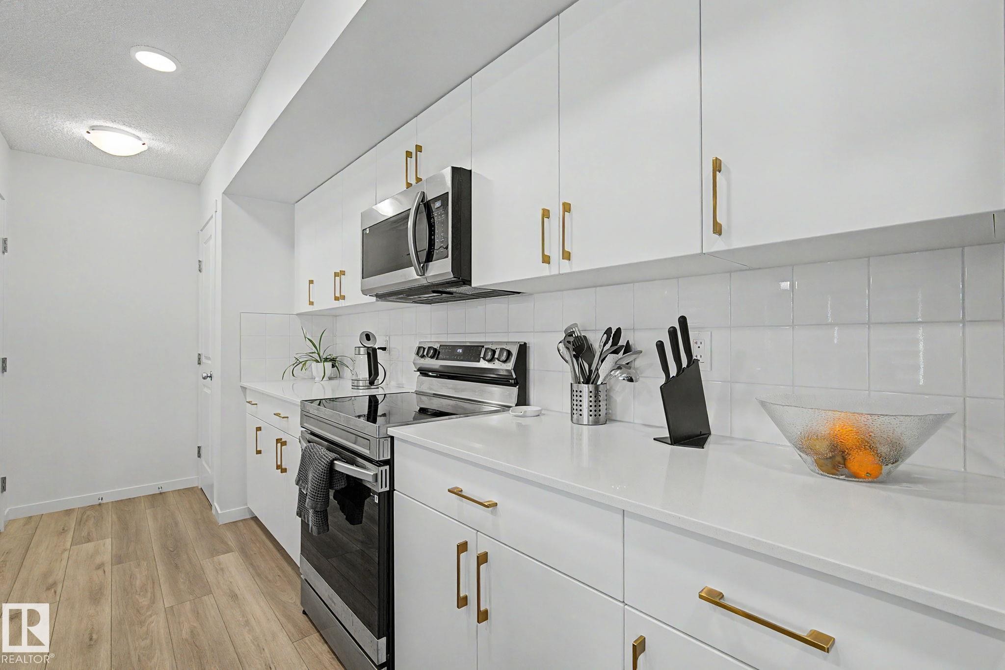Contemporary kitchen featuring white flat-panel cabinetry with gold-tone hardware, white countertops, and a white subway tile backsplash - #12 905 172 St Sw, Edmonton, AB - Indoor Photo Showing Kitchen With Upgraded Kitchen