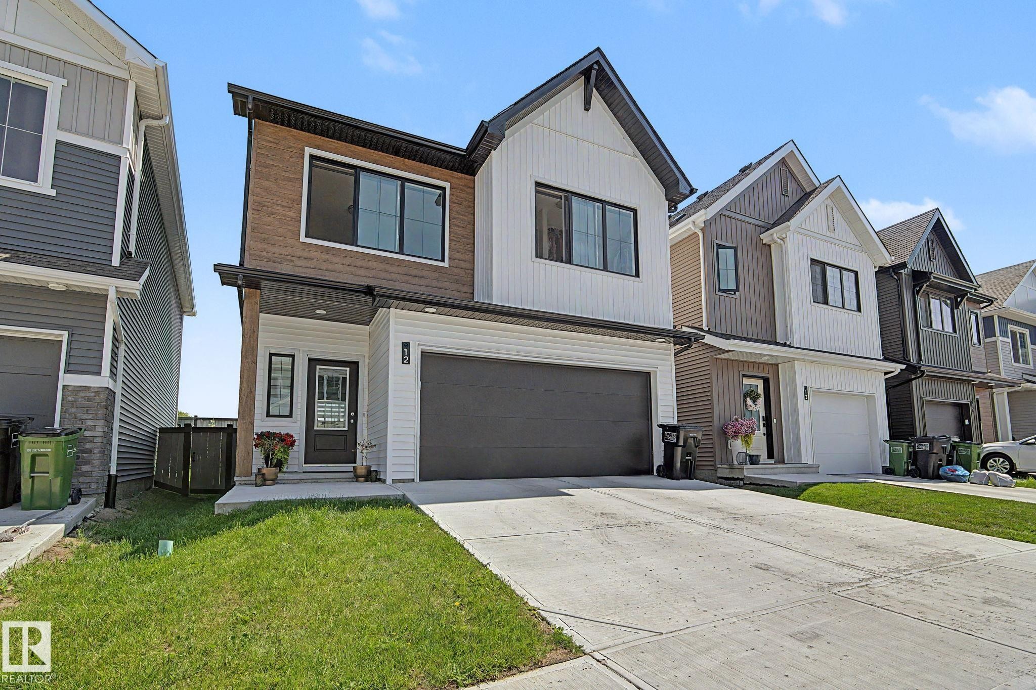 Modern two-story residence featuring a two-car garage, white siding, wood-finish paneling, black-framed windows, and a concrete driveway - #12 905 172 St Sw, Edmonton, AB - Outdoor With Facade