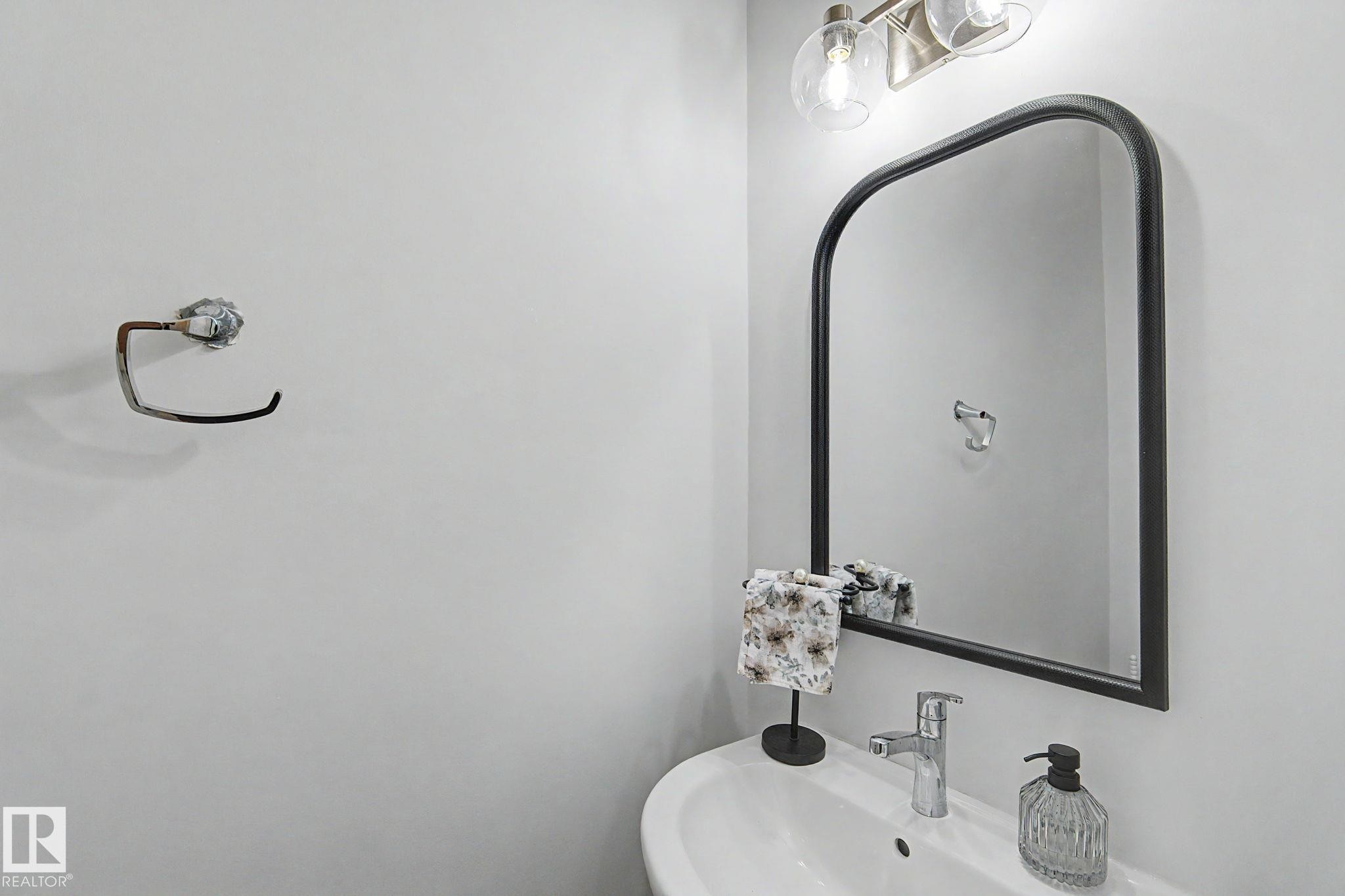 White pedestal sink with a chrome single-handle faucet, complemented by an arched black-framed mirror - #12 905 172 St Sw, Edmonton, AB - Indoor Photo Showing Bathroom