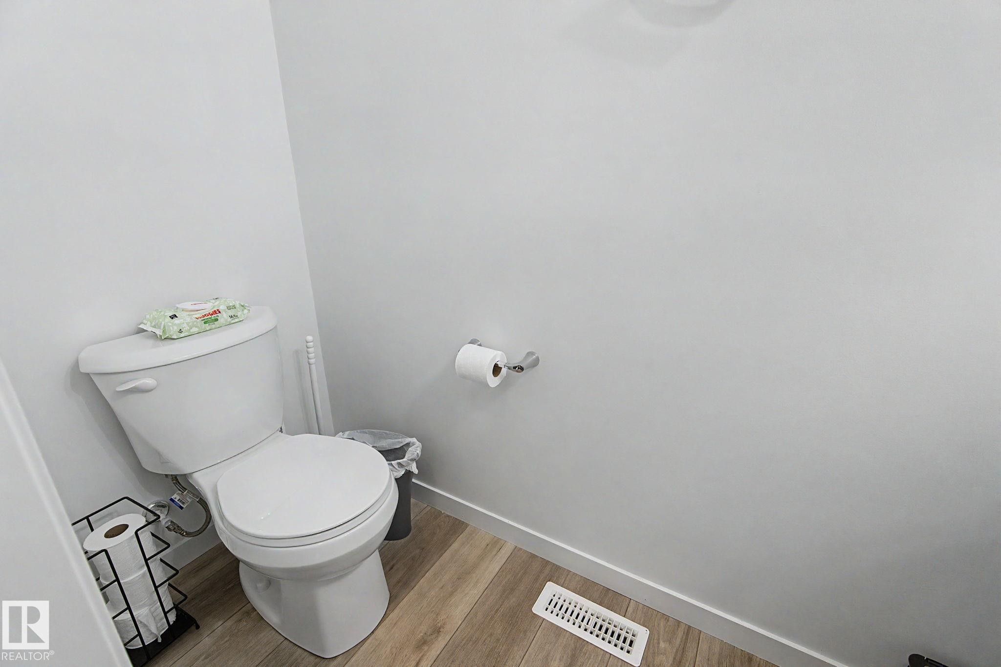 White toilet with chrome flush lever, wood-finish flooring, white baseboards, white walls, and a chrome toilet paper holder - #12 905 172 St Sw, Edmonton, AB - Indoor Photo Showing Bathroom