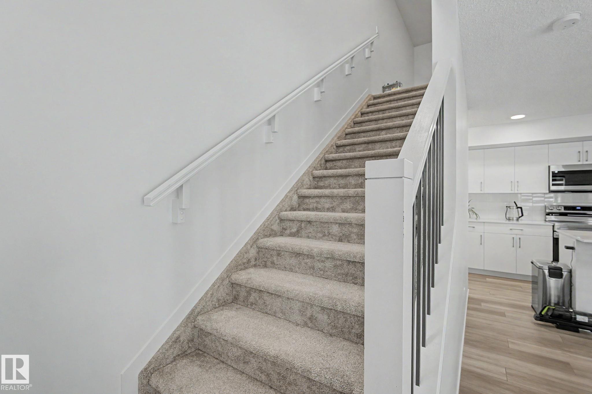 Carpeted staircase with white handrail and modern black metal balusters - #12 905 172 St Sw, Edmonton, AB - Indoor