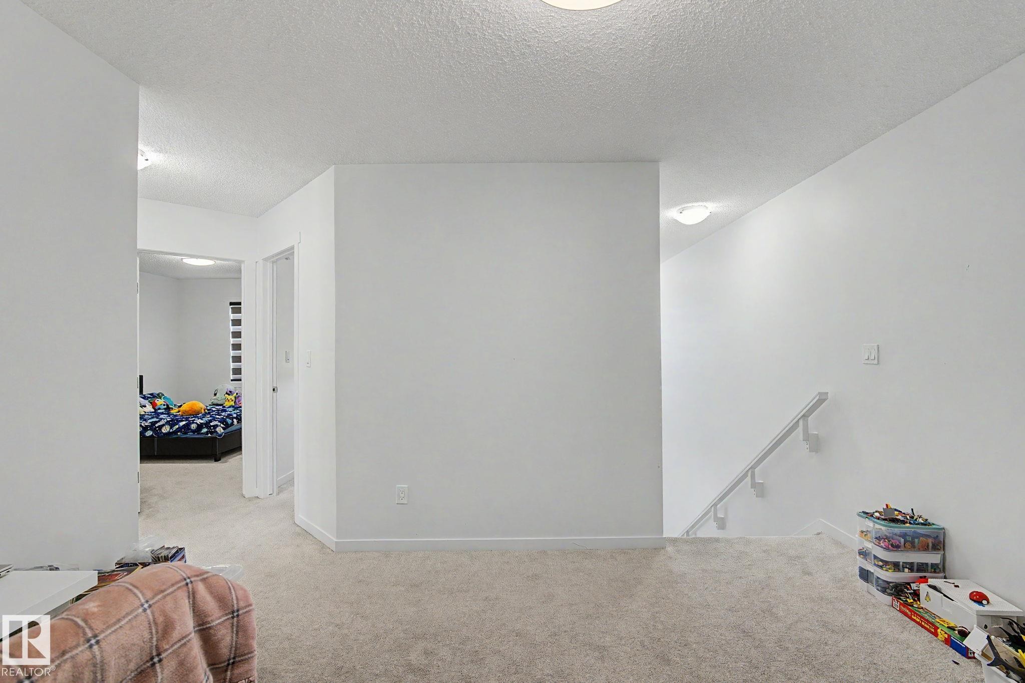 Carpeted landing featuring white walls, a white ceiling with flush-mount lighting, and a white handrail leading to a lower level - #12 905 172 St Sw, Edmonton, AB - Indoor Photo Showing Other Room