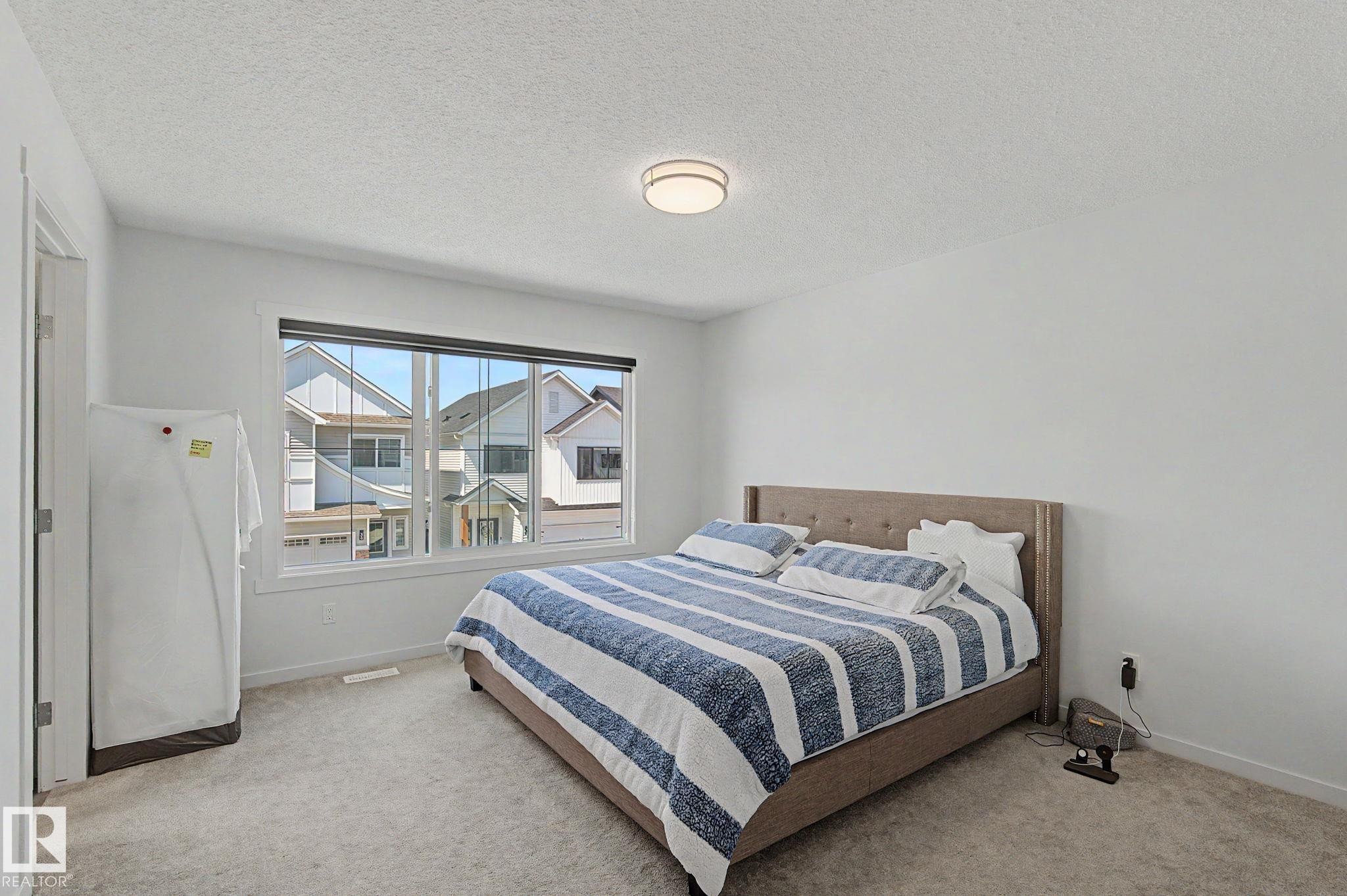 Bedroom featuring a large window with white trim, neutral-toned walls, and soft carpeting - #12 905 172 St Sw, Edmonton, AB - Indoor Photo Showing Bedroom