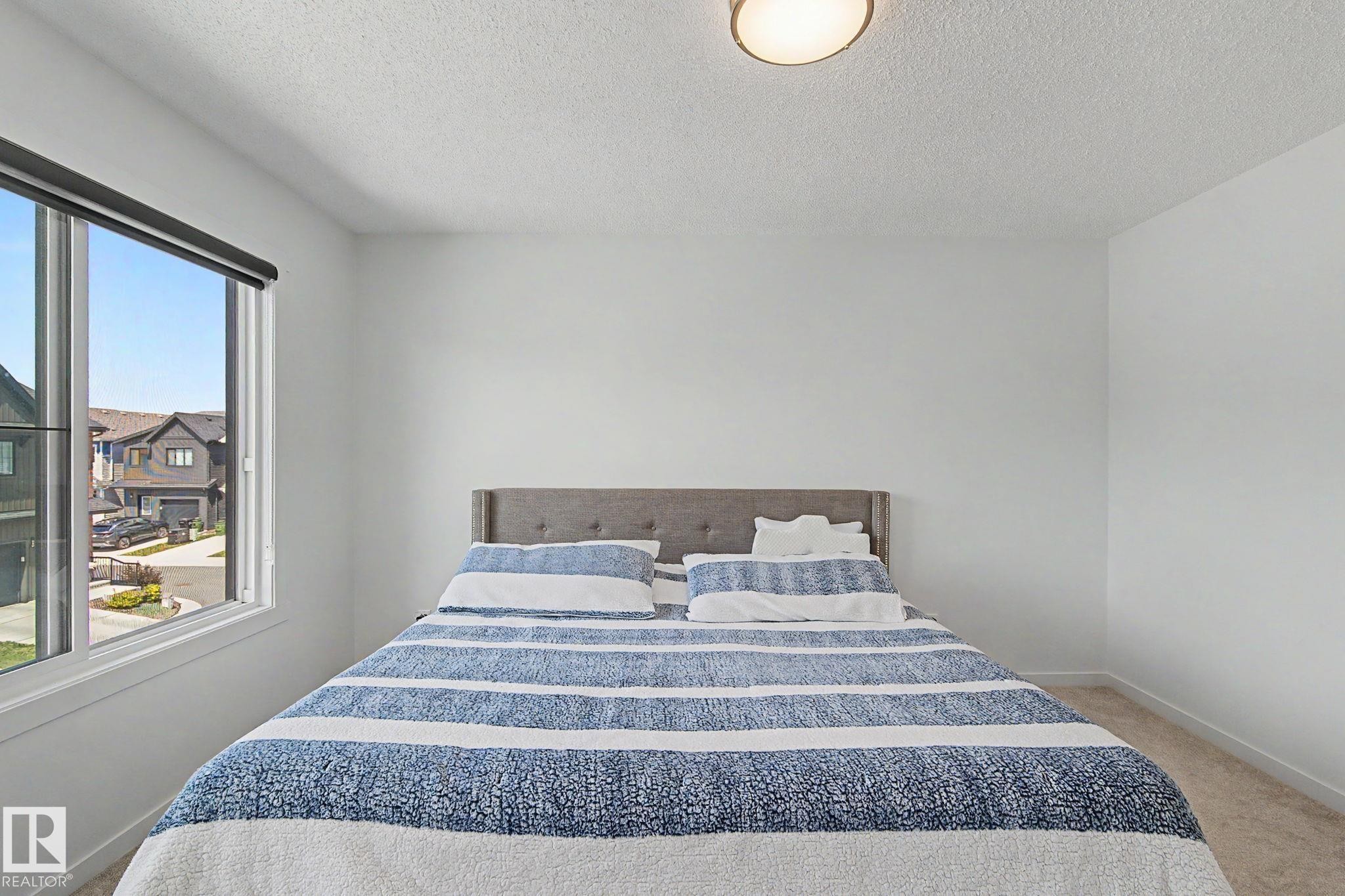 Bright room featuring a large window, neutral wall paint, and a textured ceiling - #12 905 172 St Sw, Edmonton, AB - Indoor Photo Showing Bedroom