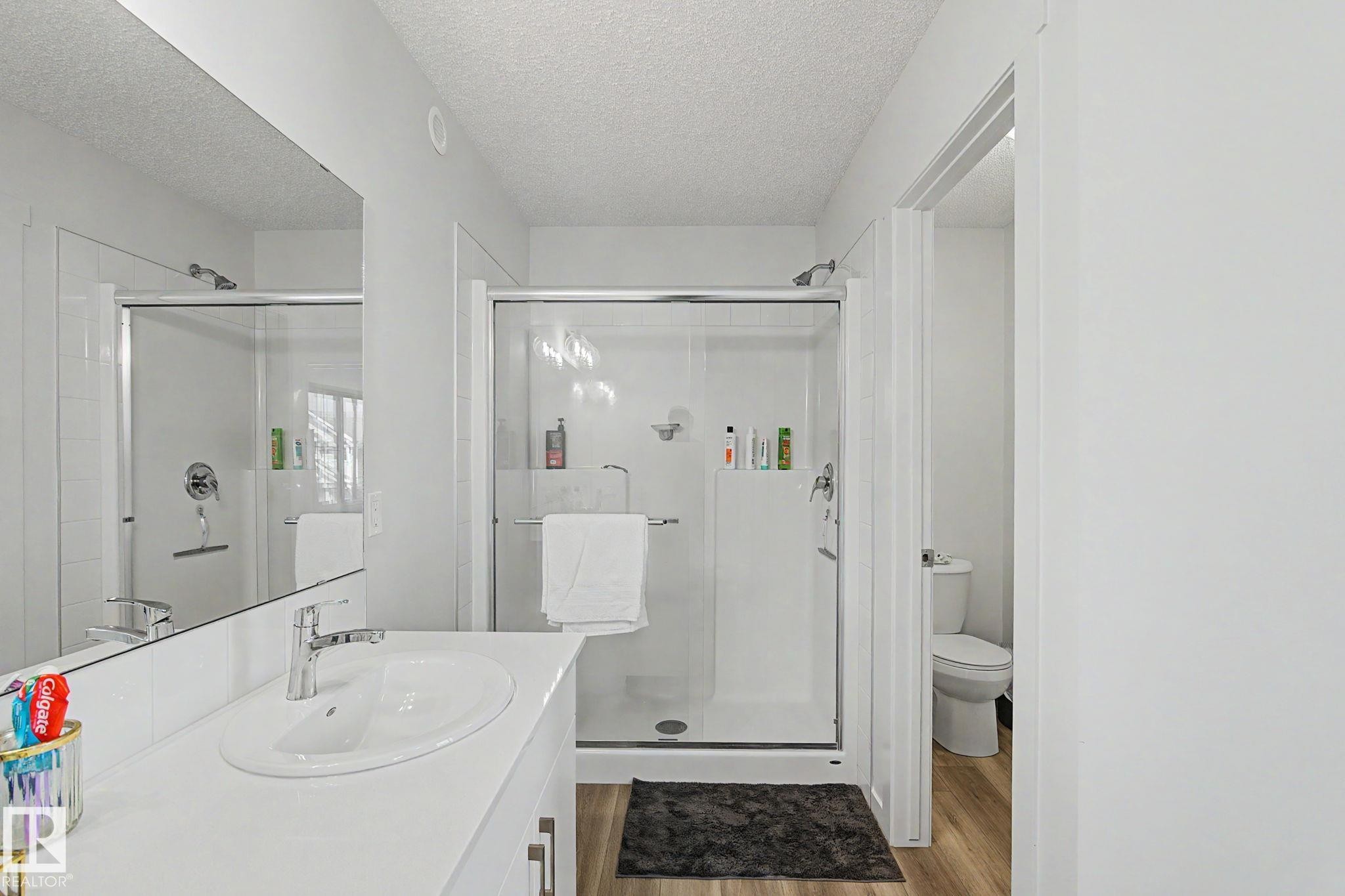 Bathroom featuring a contemporary shower with glass enclosure, single vanity with integrated sink, chrome faucet, and wood-finish flooring - #12 905 172 St Sw, Edmonton, AB - Indoor Photo Showing Bathroom