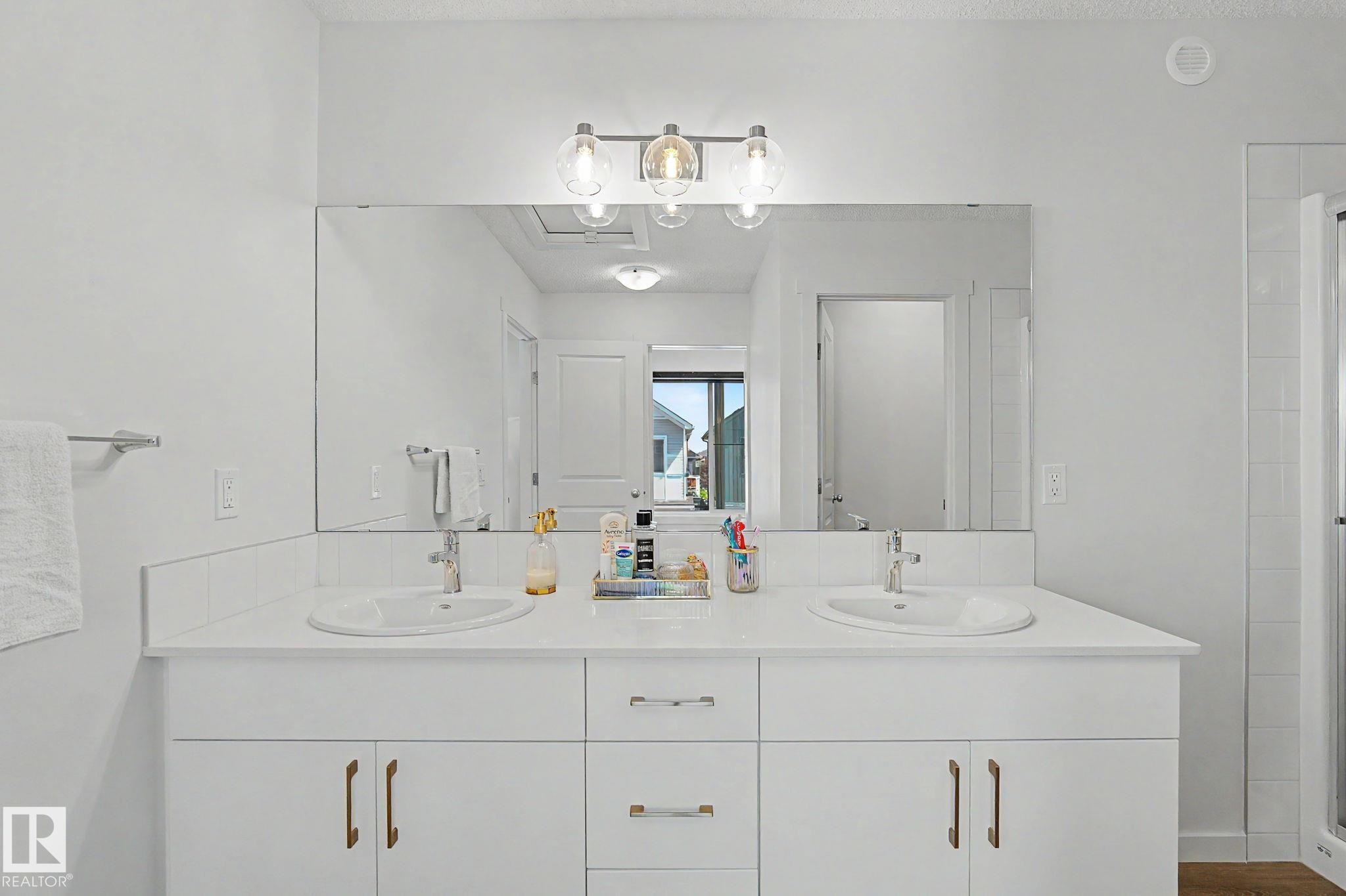 Dual vanity featuring undermount sinks, a white countertop, and white cabinetry with brass-finish hardware - #12 905 172 St Sw, Edmonton, AB - Indoor Photo Showing Bathroom