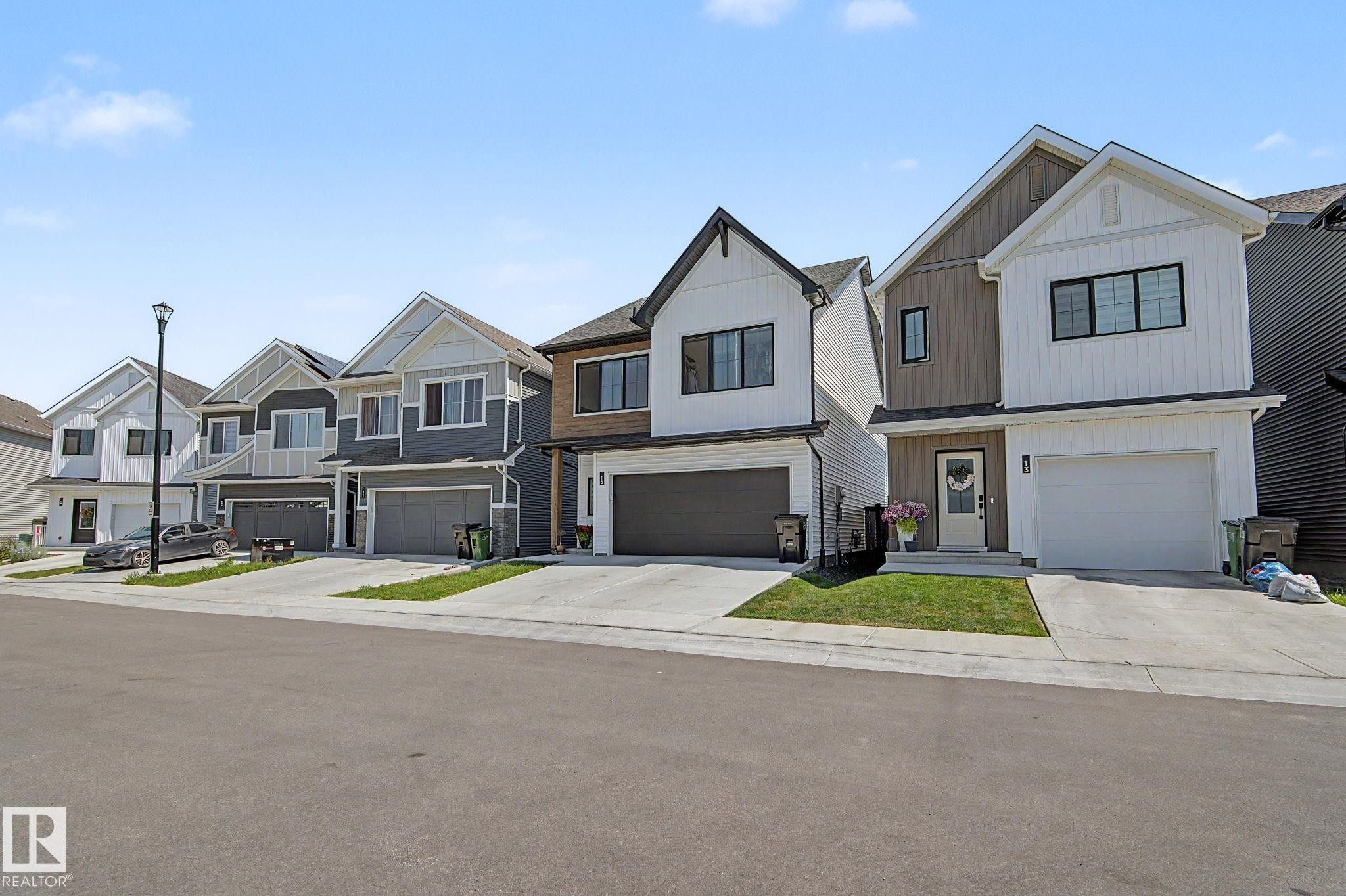 Contemporary two-story exterior featuring white and brown siding, a prominent attached garage with a white door, black-framed windows, and a concrete driveway - #12 905 172 St Sw, Edmonton, AB - Outdoor With Facade