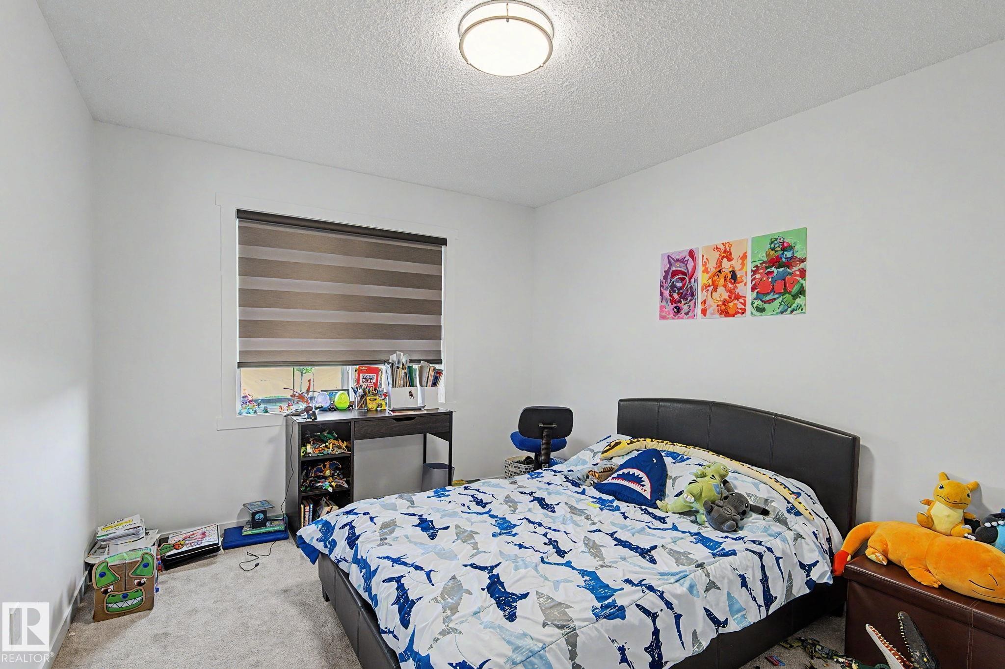 Carpeted bedroom with a window featuring horizontal blinds, a ceiling-mounted light fixture, and white painted walls - #12 905 172 St Sw, Edmonton, AB - Indoor Photo Showing Bedroom