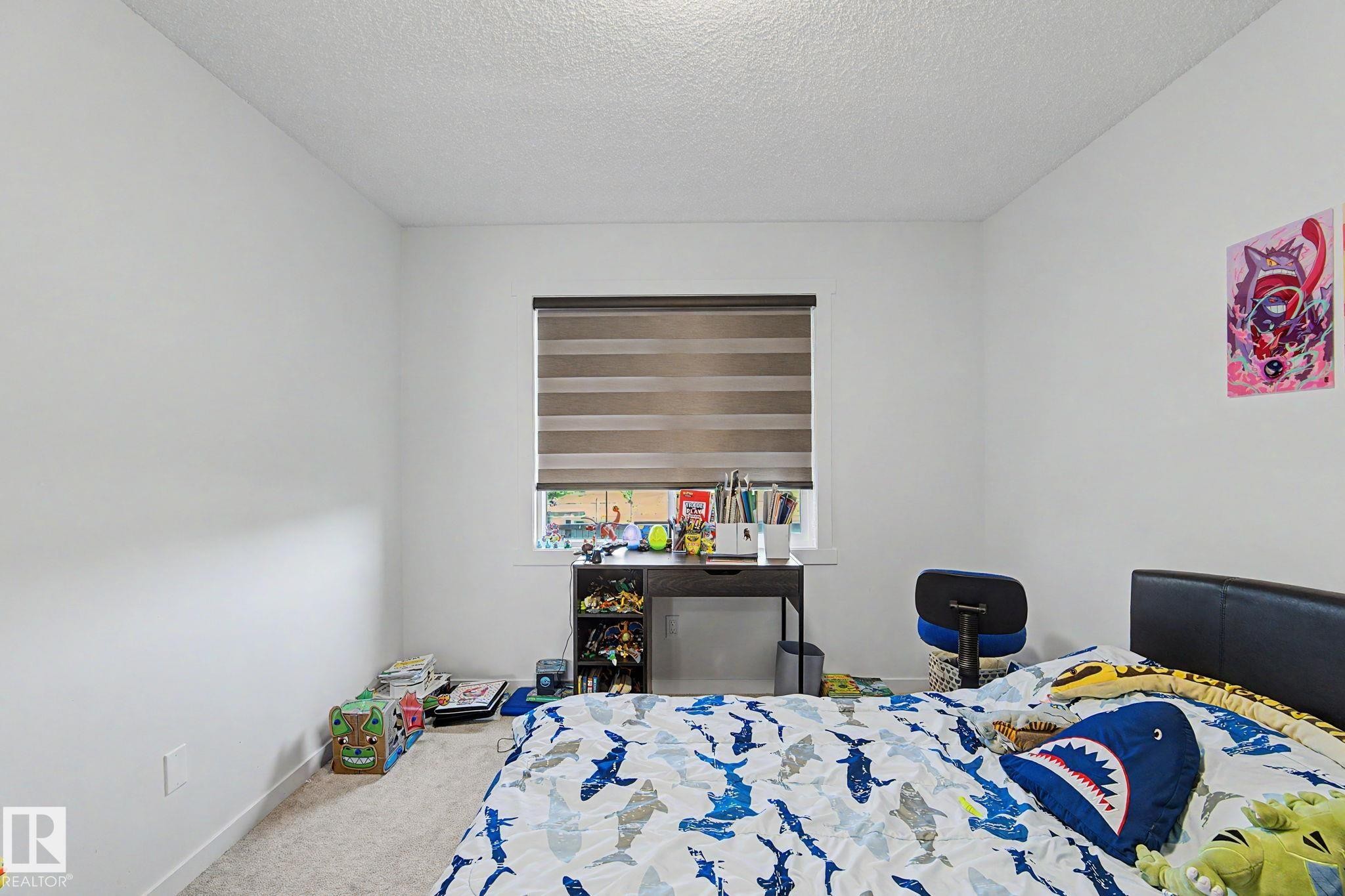 Carpeted bedroom with neutral white walls and a window featuring horizontal blinds - #12 905 172 St Sw, Edmonton, AB - Indoor Photo Showing Bedroom