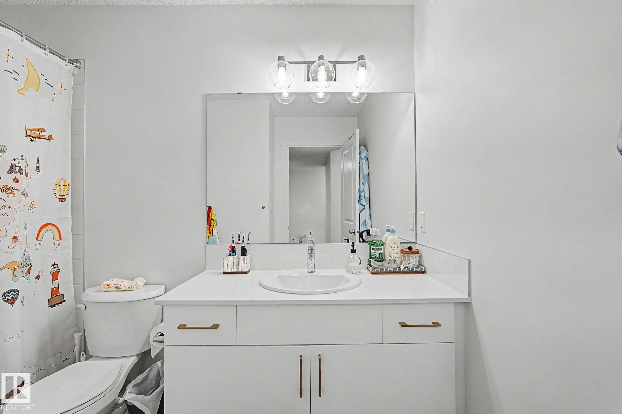 Bathroom featuring a white vanity with gold-tone hardware, an integrated sink, and a large wall mirror - #12 905 172 St Sw, Edmonton, AB - Indoor Photo Showing Bathroom
