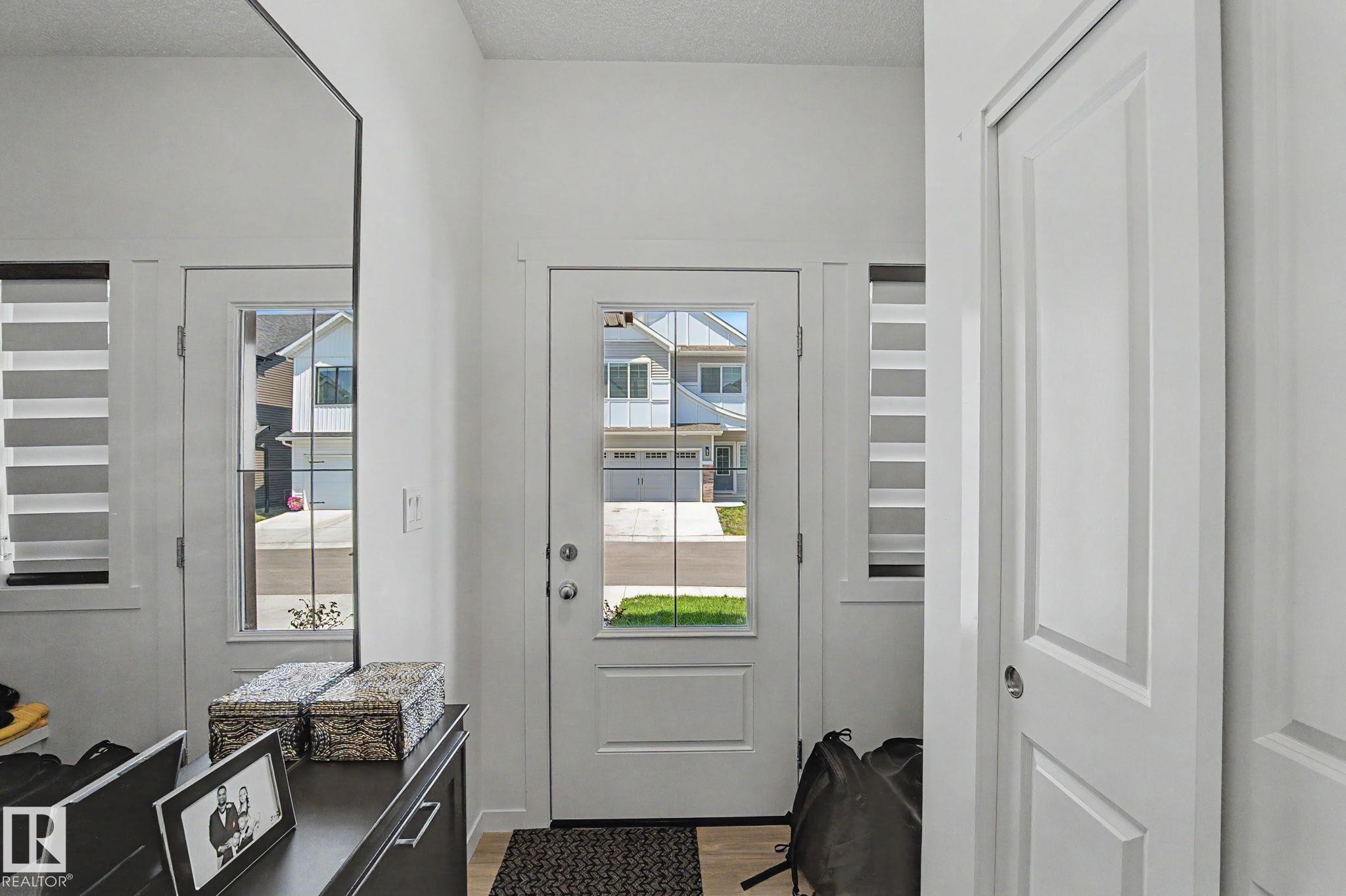 Entryway featuring a glass-paneled door, two sidelight windows with horizontal blinds, and light wood-finish flooring - #12 905 172 St Sw, Edmonton, AB - Indoor