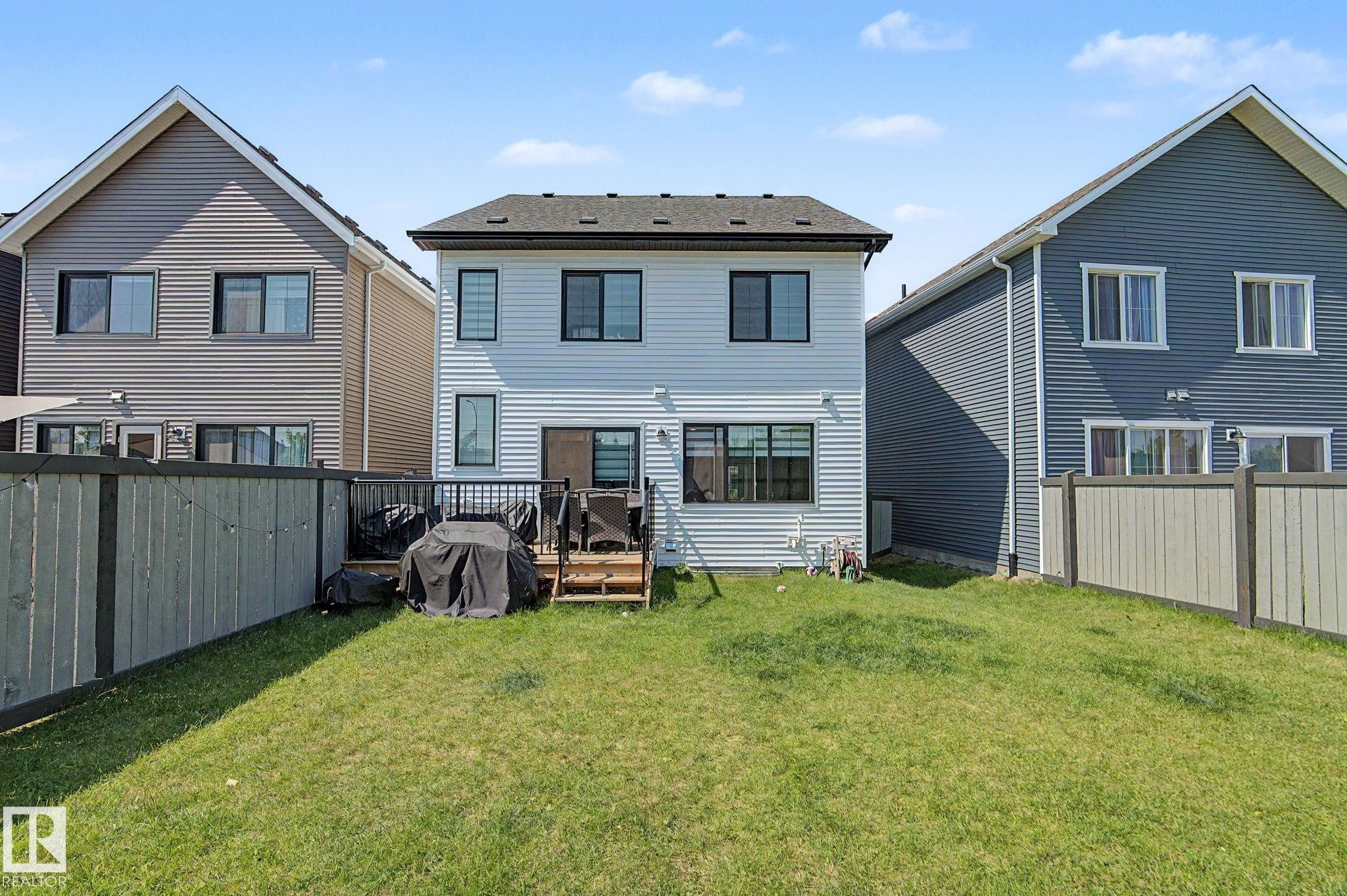 Expansive rear yard featuring a wooden privacy fence and a raised deck with black metal railings - #12 905 172 St Sw, Edmonton, AB - Outdoor