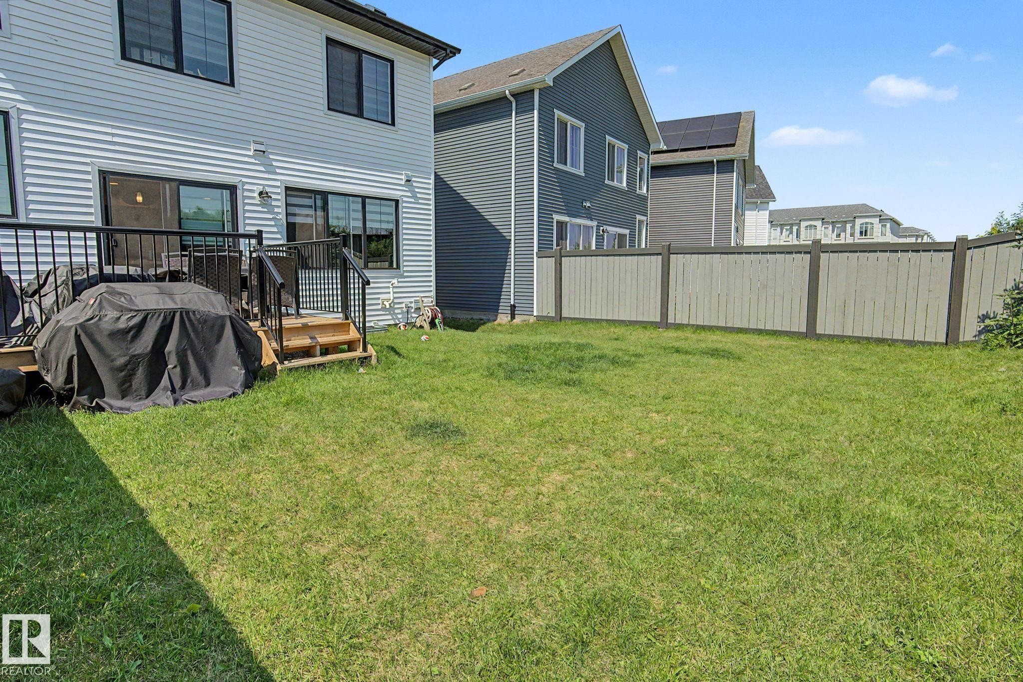 Expansive rear yard featuring a manicured lawn, full privacy fencing, and a wooden deck with black metal railings - #12 905 172 St Sw, Edmonton, AB - Outdoor