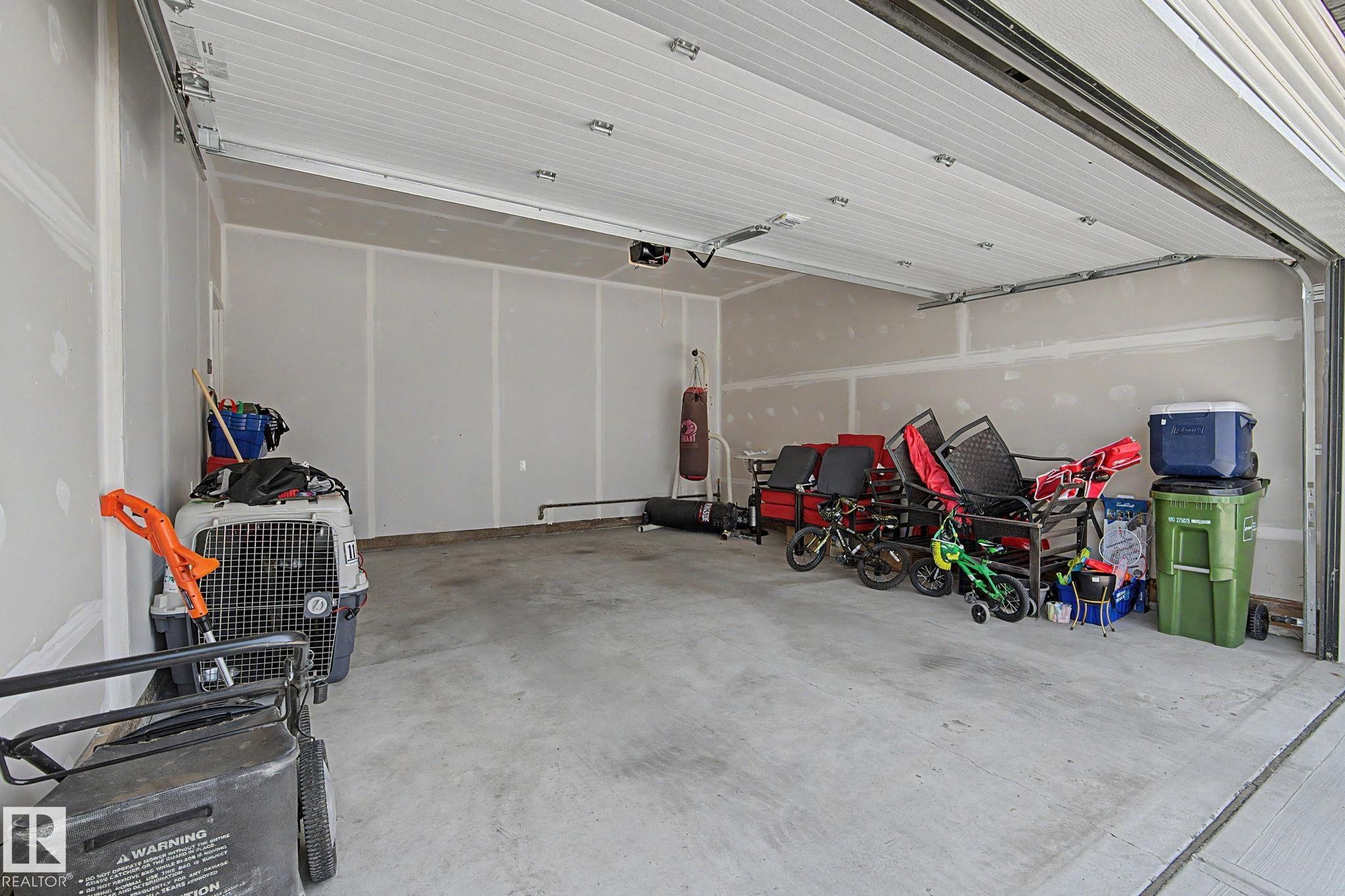 Spacious garage featuring a concrete floor, light-toned walls, and an overhead garage door - #12 905 172 St Sw, Edmonton, AB - Indoor Photo Showing Garage