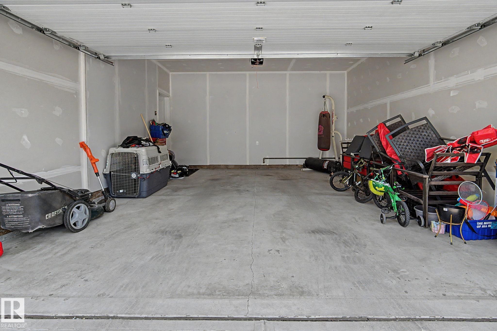 Spacious two-car garage featuring a concrete floor, unfinished drywall, and an overhead garage door mechanism - #12 905 172 St Sw, Edmonton, AB - Indoor Photo Showing Garage