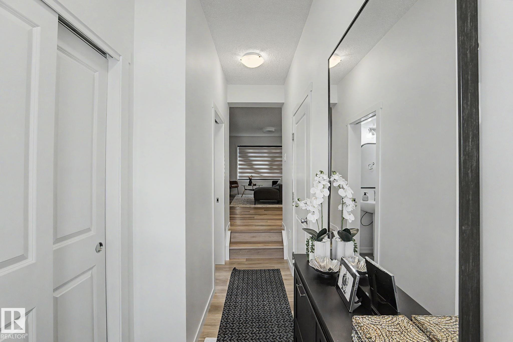 Bright hallway featuring wood-finish flooring, white walls, and a contemporary ceiling light fixture - #12 905 172 St Sw, Edmonton, AB - Indoor Photo Showing Other Room