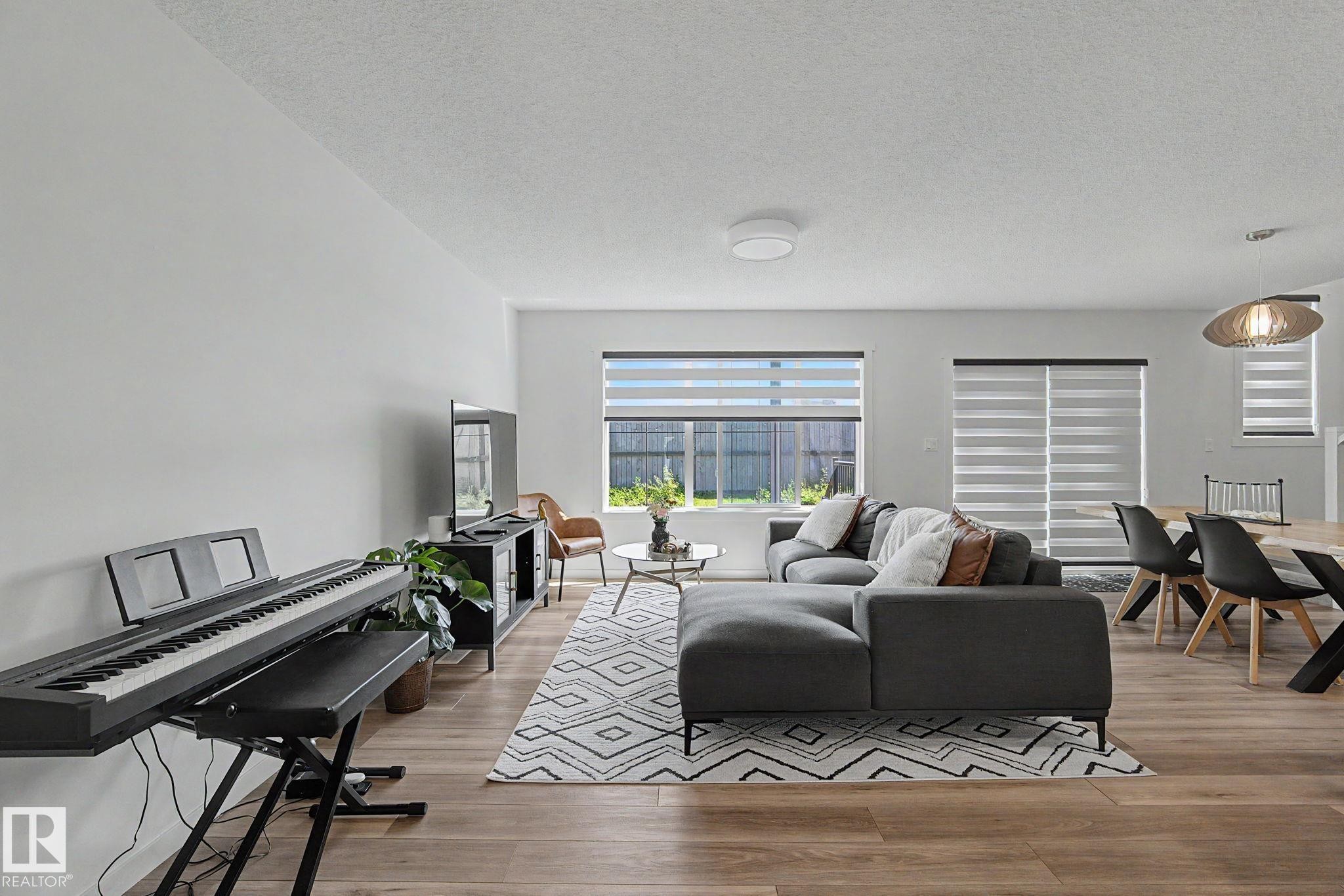 Open-concept living space featuring wood-finish flooring, white walls, and multiple windows with horizontal blinds - #12 905 172 St Sw, Edmonton, AB - Indoor Photo Showing Living Room