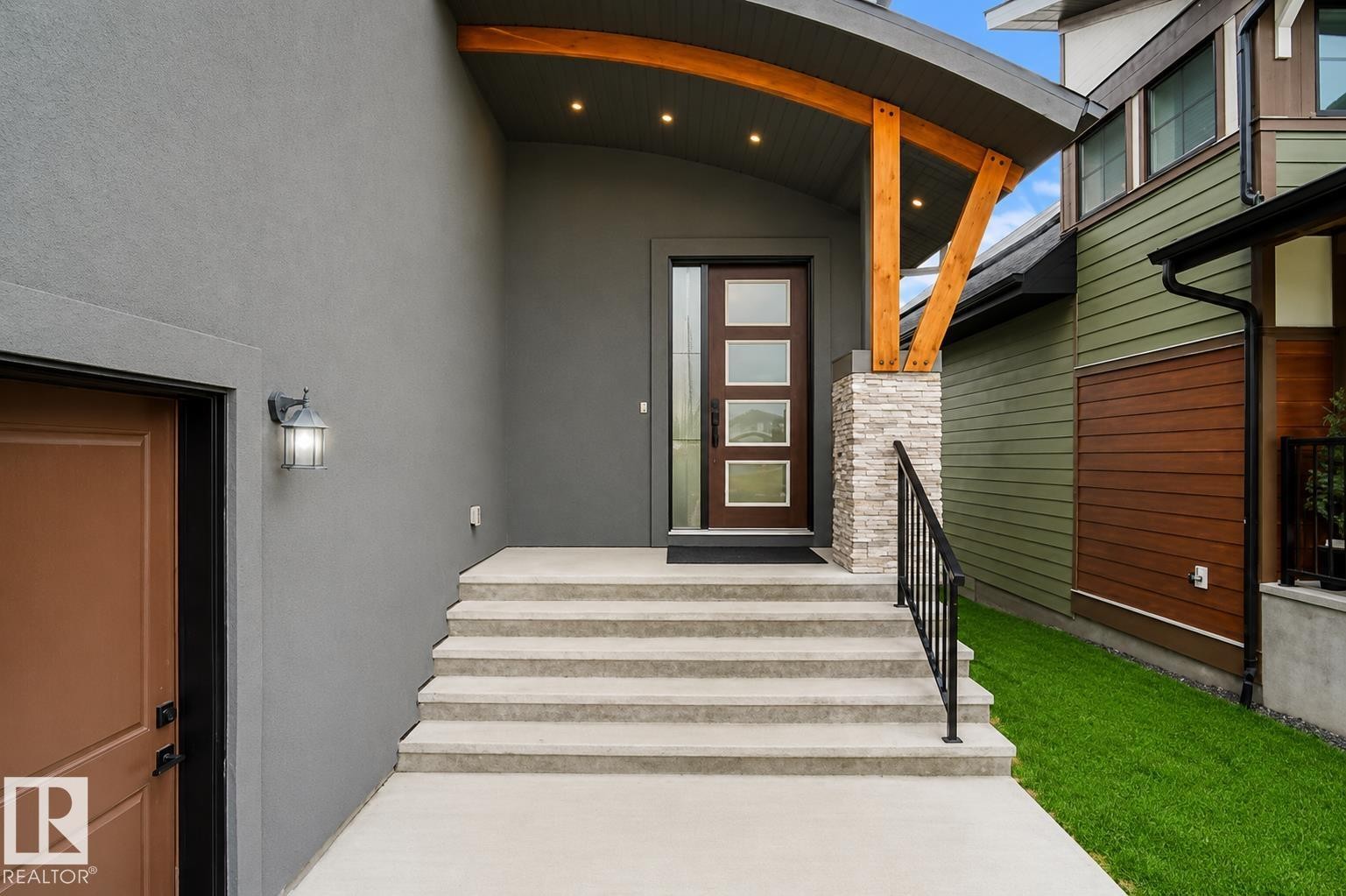 Curved portico with exposed wood beams, stone pillar, concrete steps, and a contemporary entry door with frosted glass panels - 162 Edgewater Circle, Leduc, AB