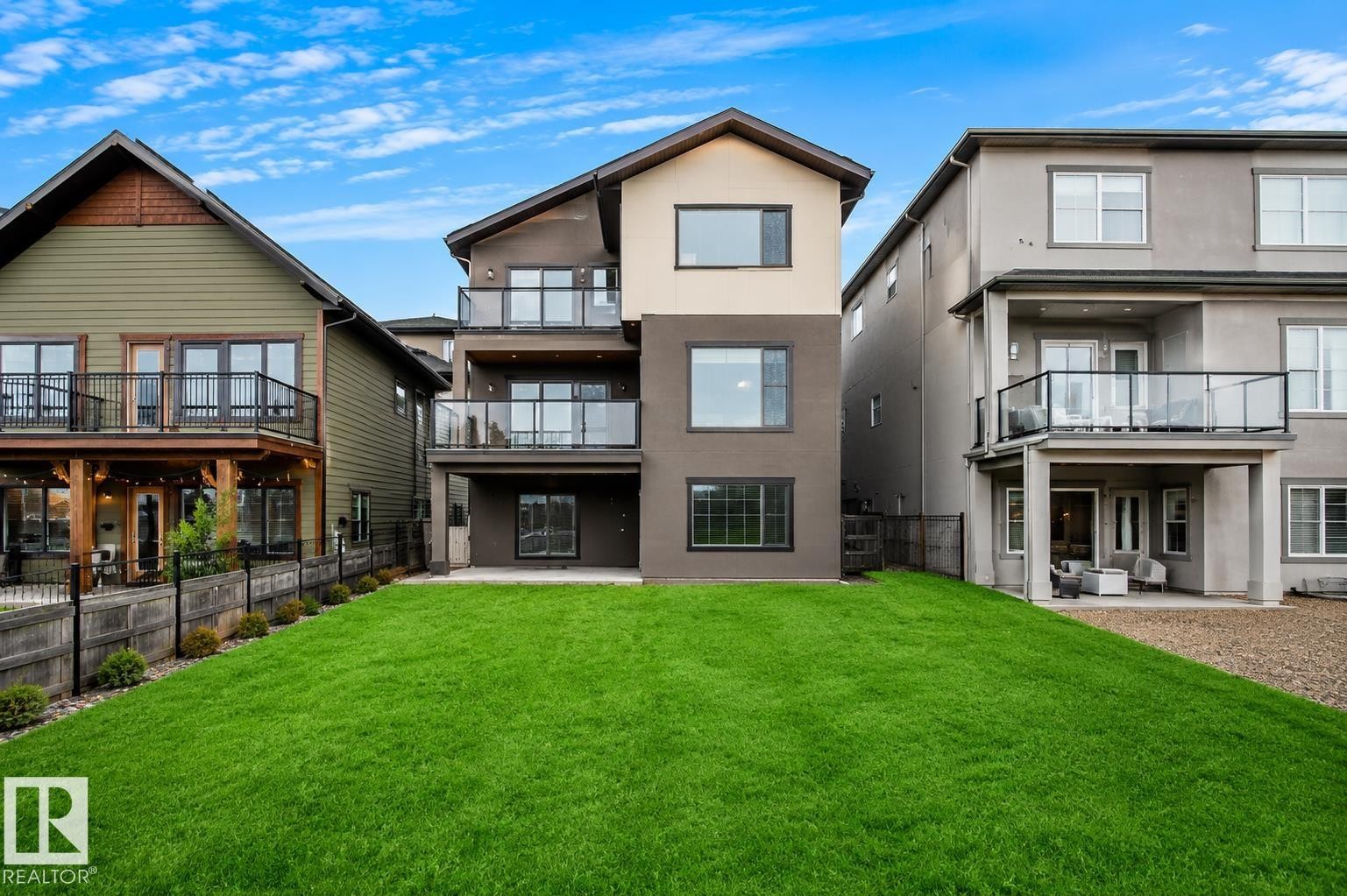 Expansive backyard featuring a manicured lawn, multi-level balconies with glass railings, and a lower-level patio - 162 Edgewater Circle, Leduc, AB