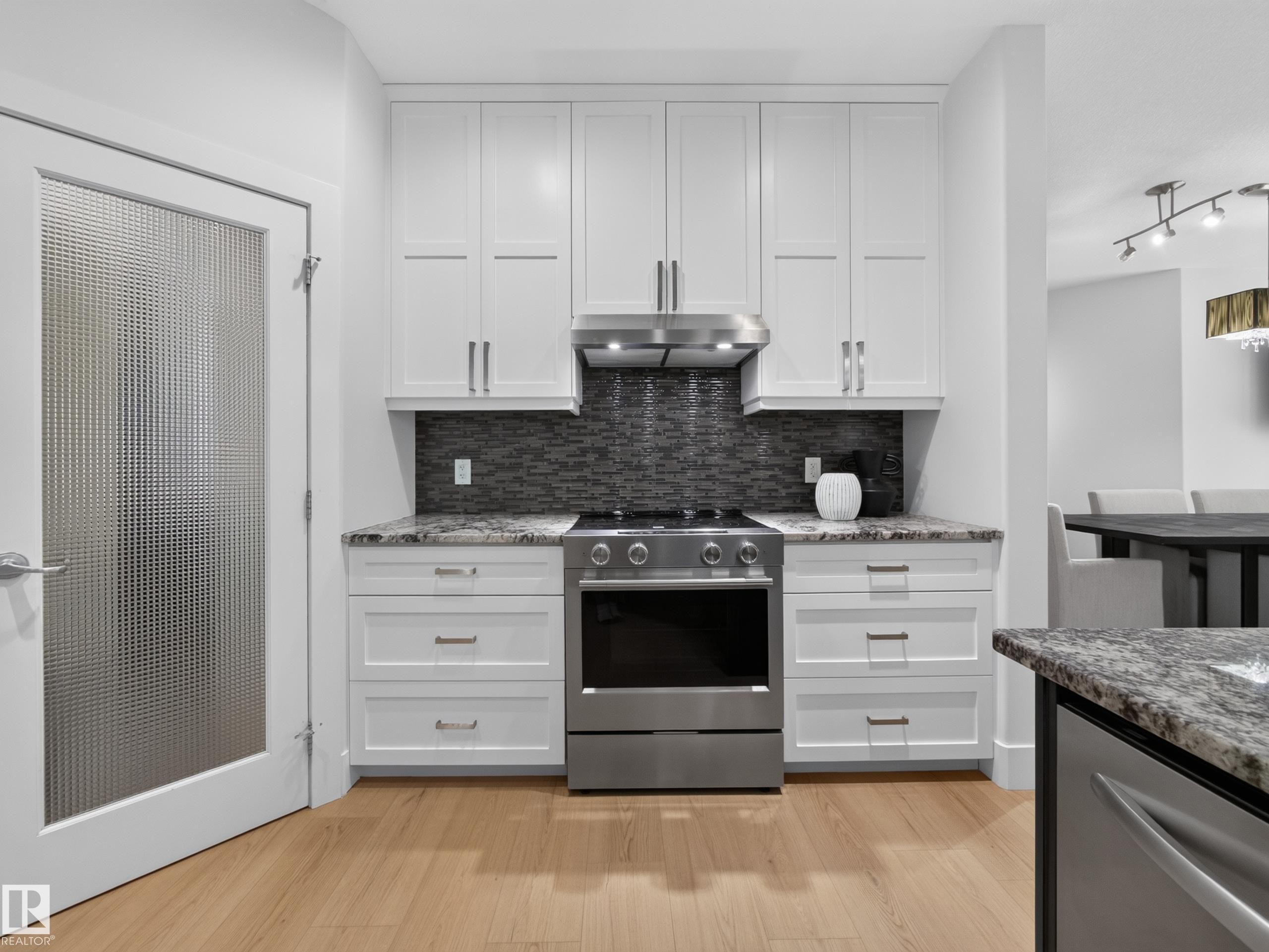 Modern kitchen featuring stainless steel appliances, granite countertops, white shaker cabinetry, and a dark mosaic tile backsplash - #59 10550 Ellerslie Rd Sw, Edmonton, AB - Indoor Photo Showing Kitchen With Upgraded Kitchen