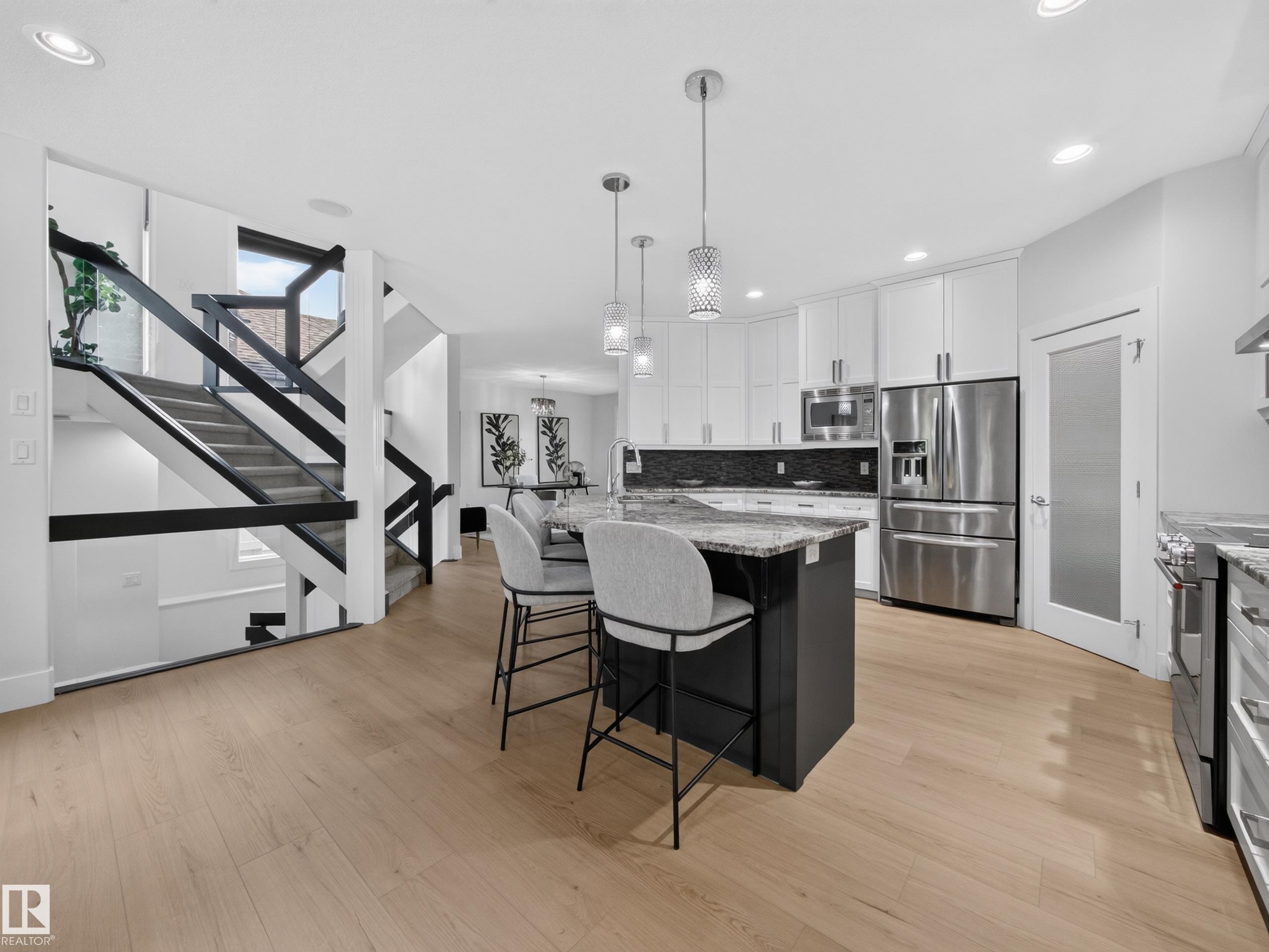 Bright kitchen featuring wood-finish flooring, a central island with a granite-style countertop, stainless steel appliances, white cabinetry, and recessed lighting - #59 10550 Ellerslie Rd Sw, Edmonton, AB - Indoor Photo Showing Kitchen With Upgraded Kitchen