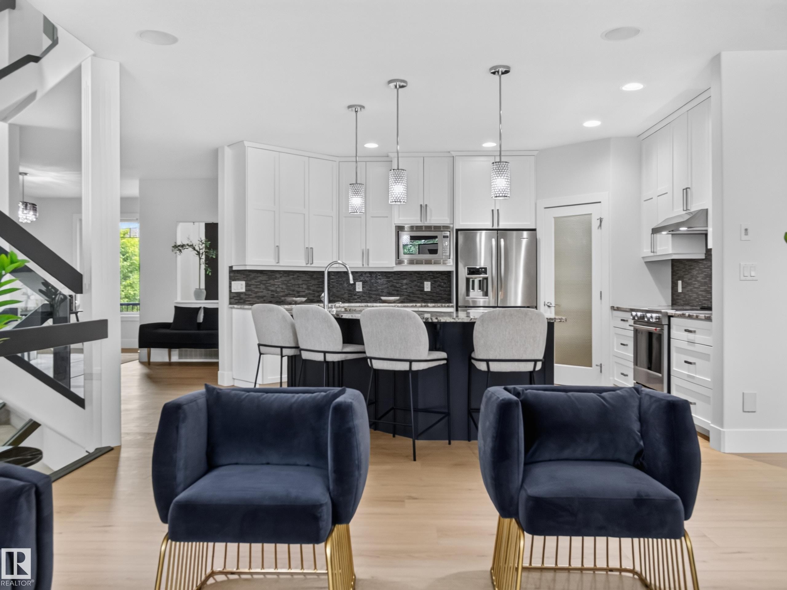 Contemporary kitchen with white shaker cabinetry, stainless steel appliances, a dark-toned island with seating, and light wood-finish flooring - #59 10550 Ellerslie Rd Sw, Edmonton, AB - Indoor