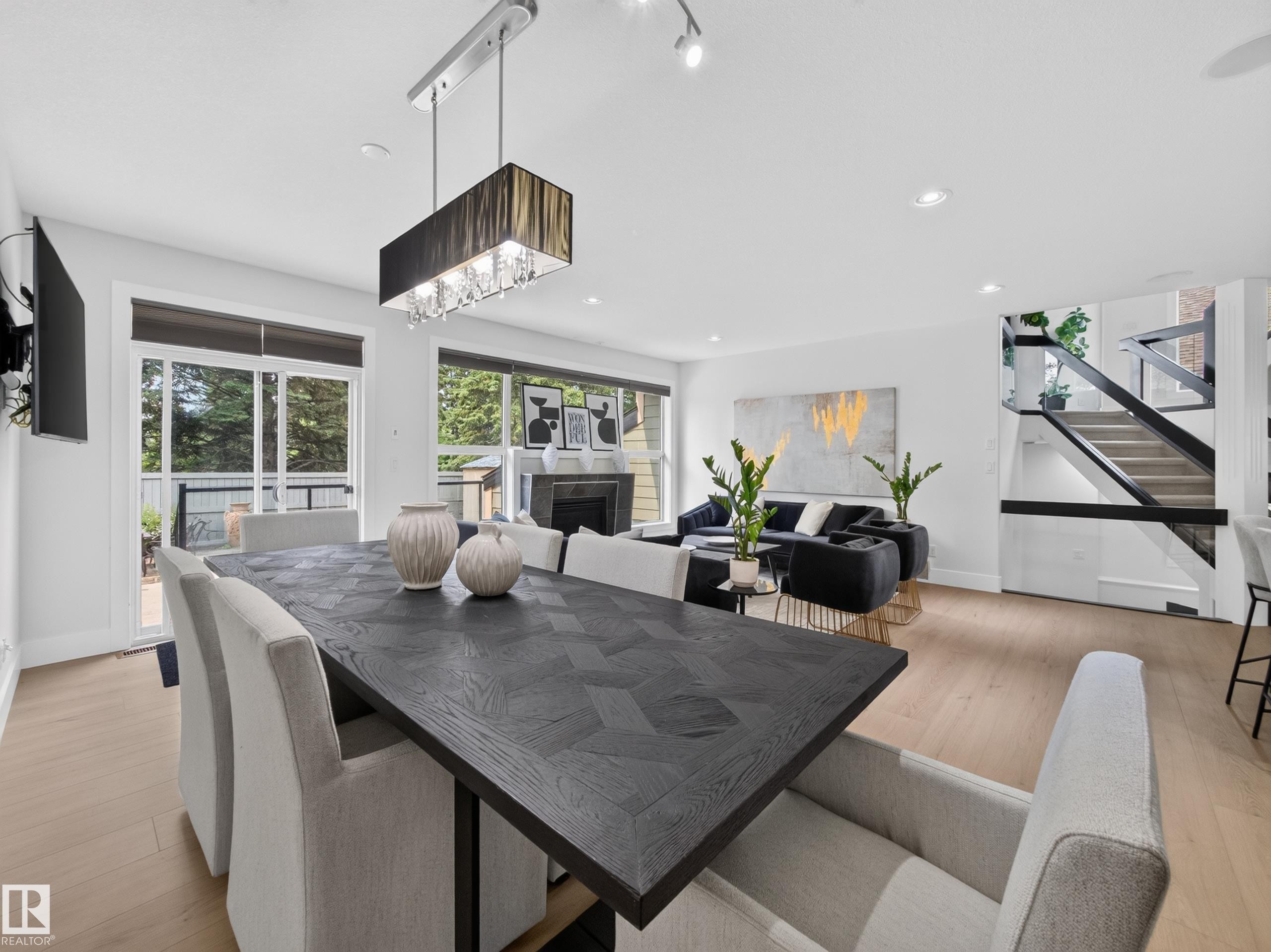 Open-concept living space featuring wood-finish flooring, a contemporary fireplace, and a striking staircase with dark railings - #59 10550 Ellerslie Rd Sw, Edmonton, AB - Indoor Photo Showing Dining Room