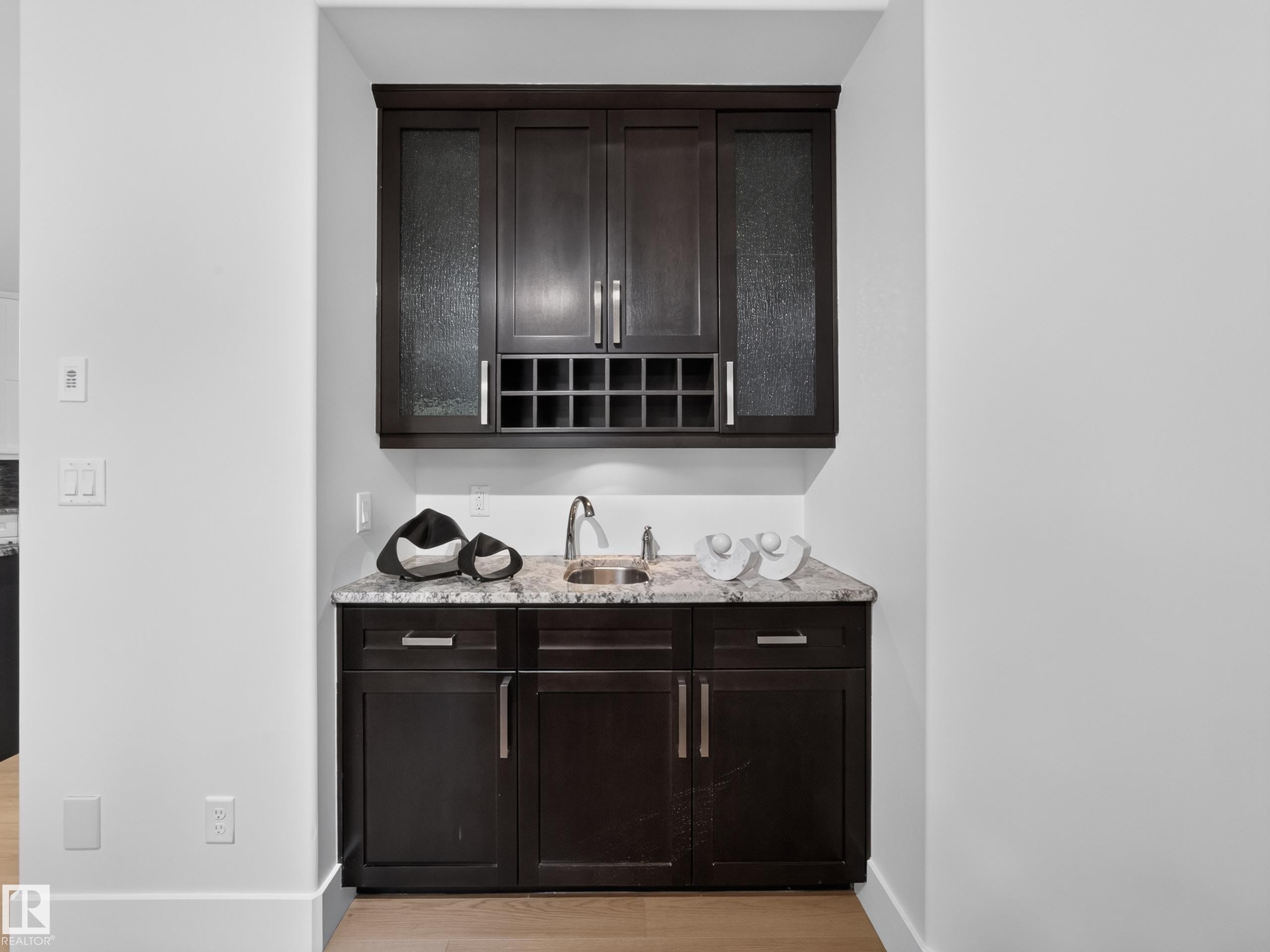 Built-in wet bar featuring dark wood cabinetry, a stone-finish countertop, stainless steel sink, and integrated wine rack - #59 10550 Ellerslie Rd Sw, Edmonton, AB - Indoor Photo Showing Other Room