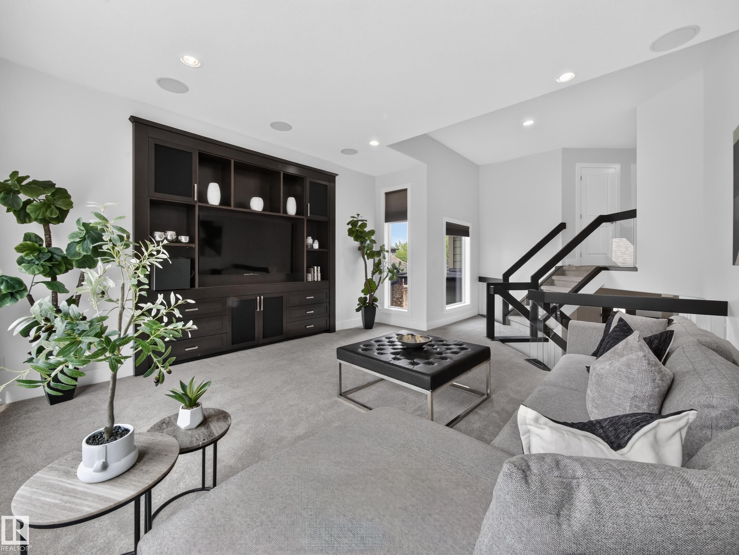 Spacious entertainment area featuring a built-in media cabinet, recessed lighting, and grey carpeting - #59 10550 Ellerslie Rd Sw, Edmonton, AB - Indoor