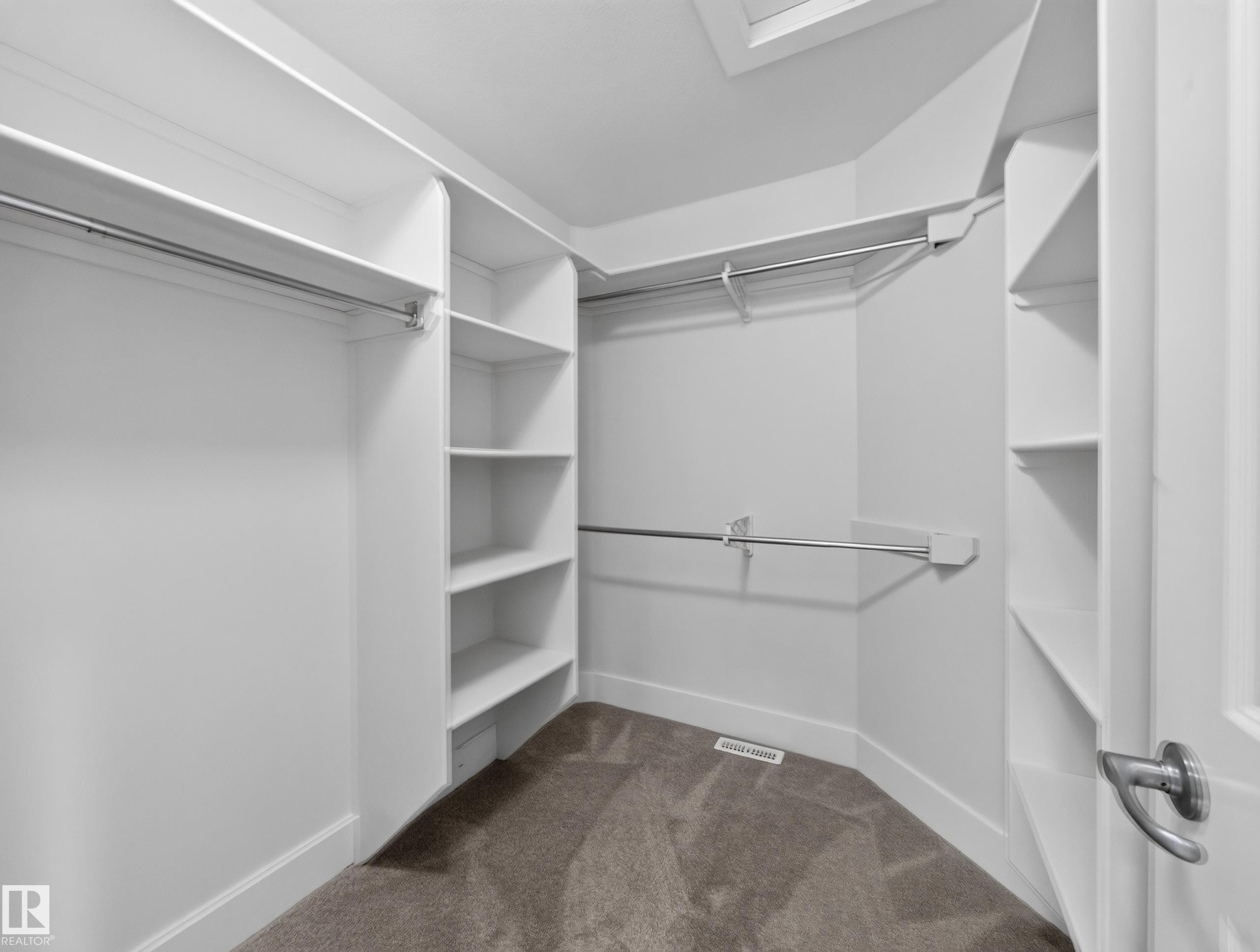 Walk-in closet featuring white built-in shelving, multiple hanging rods, white trim, and gray carpeting - #59 10550 Ellerslie Rd Sw, Edmonton, AB - Indoor With Storage