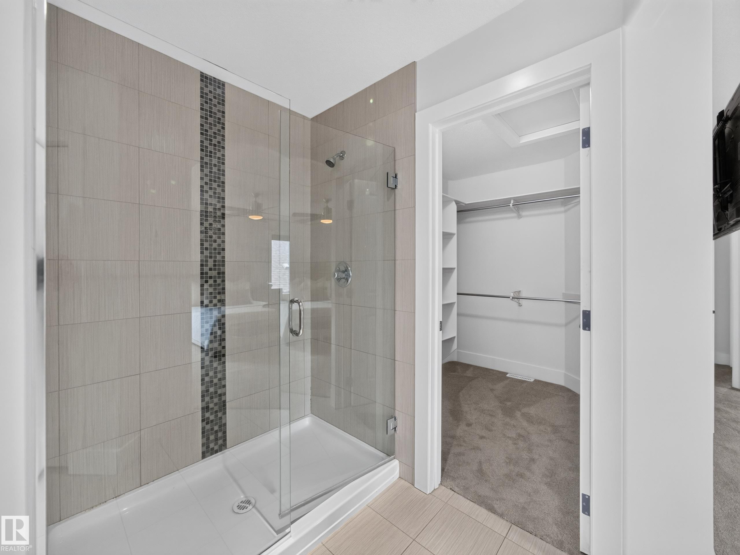 Glass-enclosed shower featuring large format wall tiles with a decorative mosaic accent strip - #59 10550 Ellerslie Rd Sw, Edmonton, AB - Indoor Photo Showing Bathroom